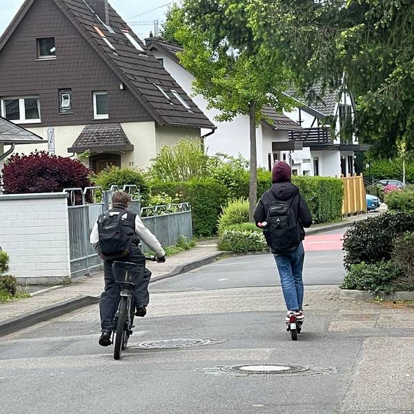 Ein Junge faährt auf dem Farrad, ein Junge auf dem Roller.