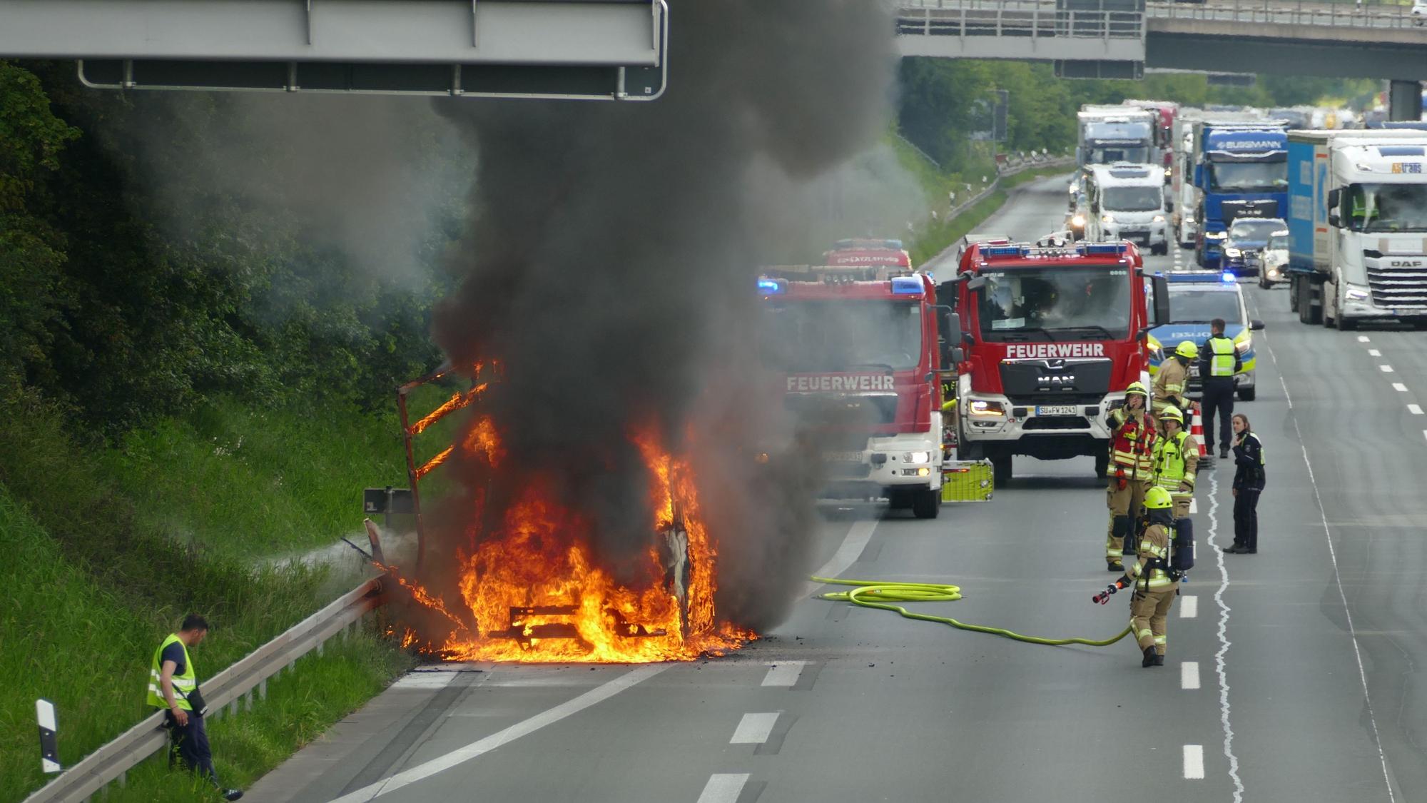 Die Aufnahme zeigt das brennende Fahrzeug und Feuerwehrleute, die mit den Löscharbeiten beginnen.