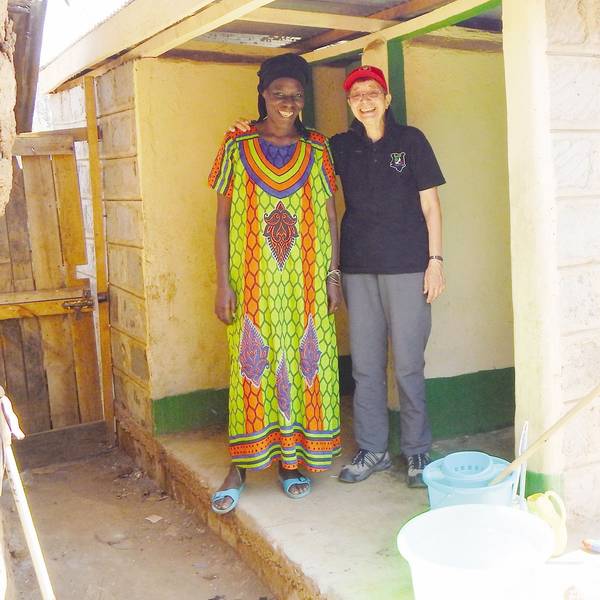 Eine Frau mit Schirmmütze legt den Arm um eine Afrikanerin im bunten Kleid.