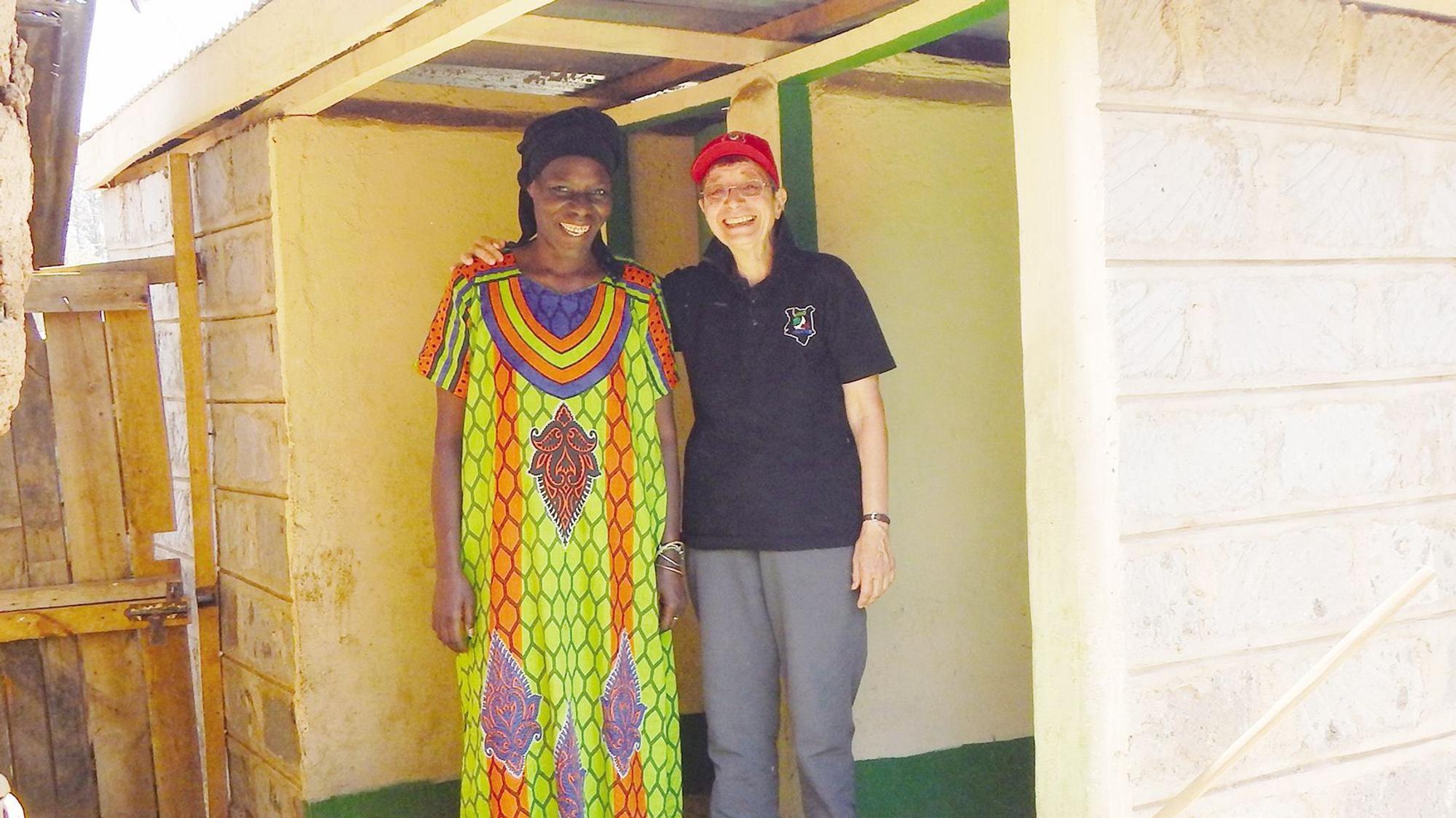 Eine Frau mit Schirmmütze legt den Arm um eine Afrikanerin im bunten Kleid.