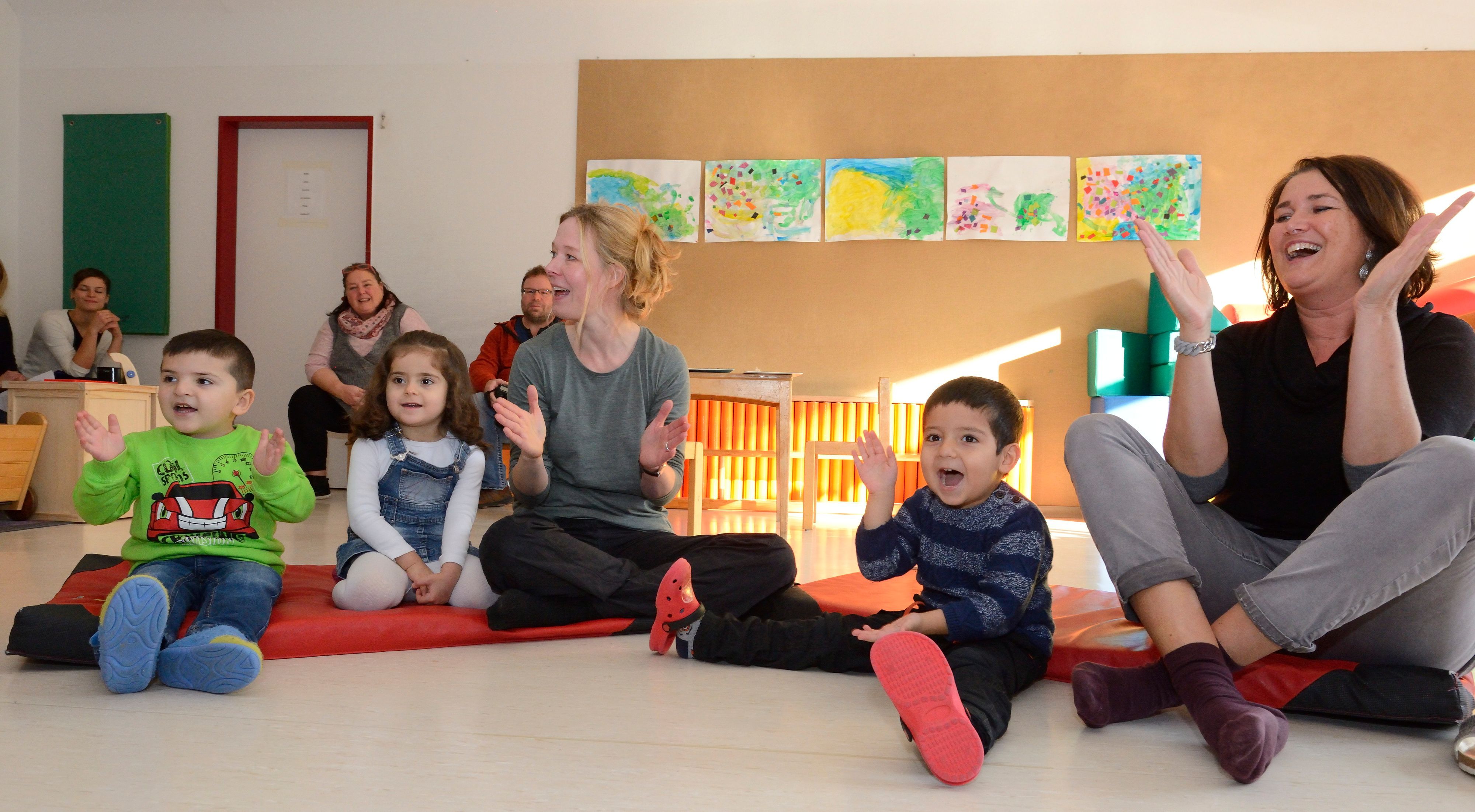 Kinder und Erzieherinnen sitzen auf dem Boden und klatschen.