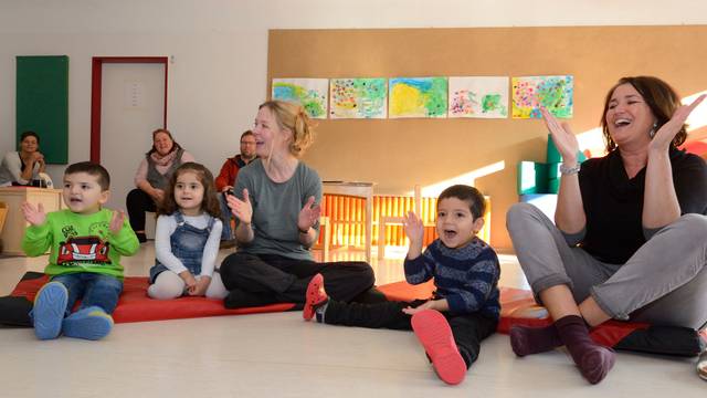 Kinder und Erzieherinnen sitzen auf dem Boden und klatschen.