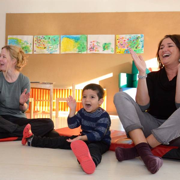Kinder und Erzieherinnen sitzen auf dem Boden und klatschen.