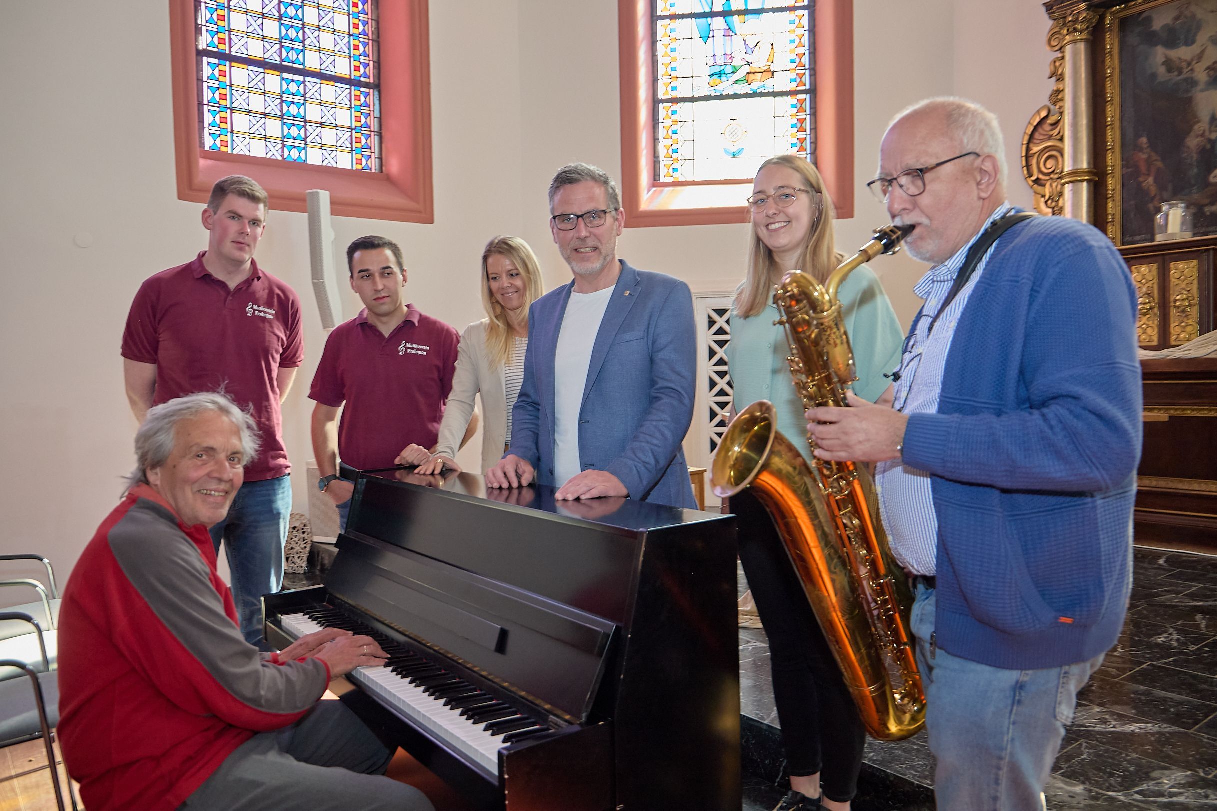 In der Klosterkapelle Nettersheim haben sich die Genannten an einem Piano aufgestellt, an dem ein Musiker sitzt. Ein Mann spielt auf einem Saxofon.