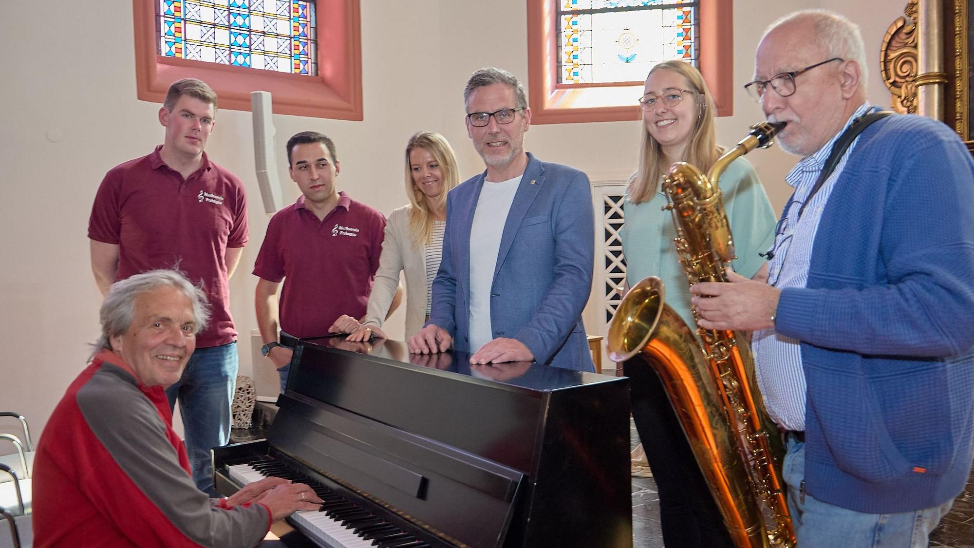 In der Klosterkapelle Nettersheim haben sich die Genannten an einem Piano aufgestellt, an dem ein Musiker sitzt. Ein Mann spielt auf einem Saxofon.