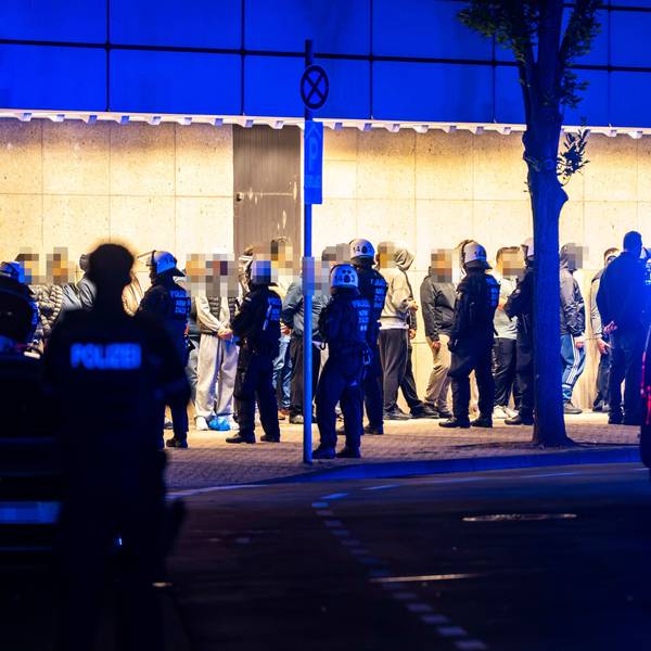 Das Bild zeigt zahlreiche Menschen, die mutmaßlich an der Schlägerei beteiligt waren. Sie werden von Polizeibeamten bewacht.