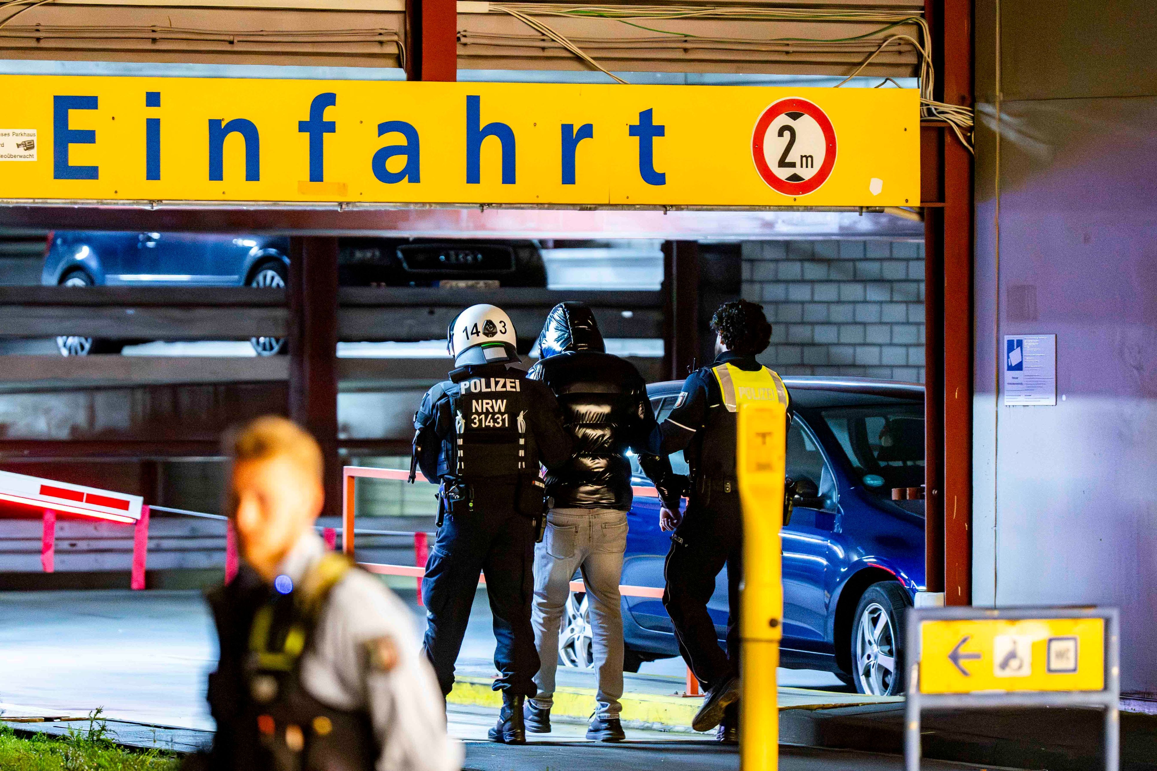 Das Bild zeigt zwei Polizisten, die einen Mann in ein Parkhaus führen.