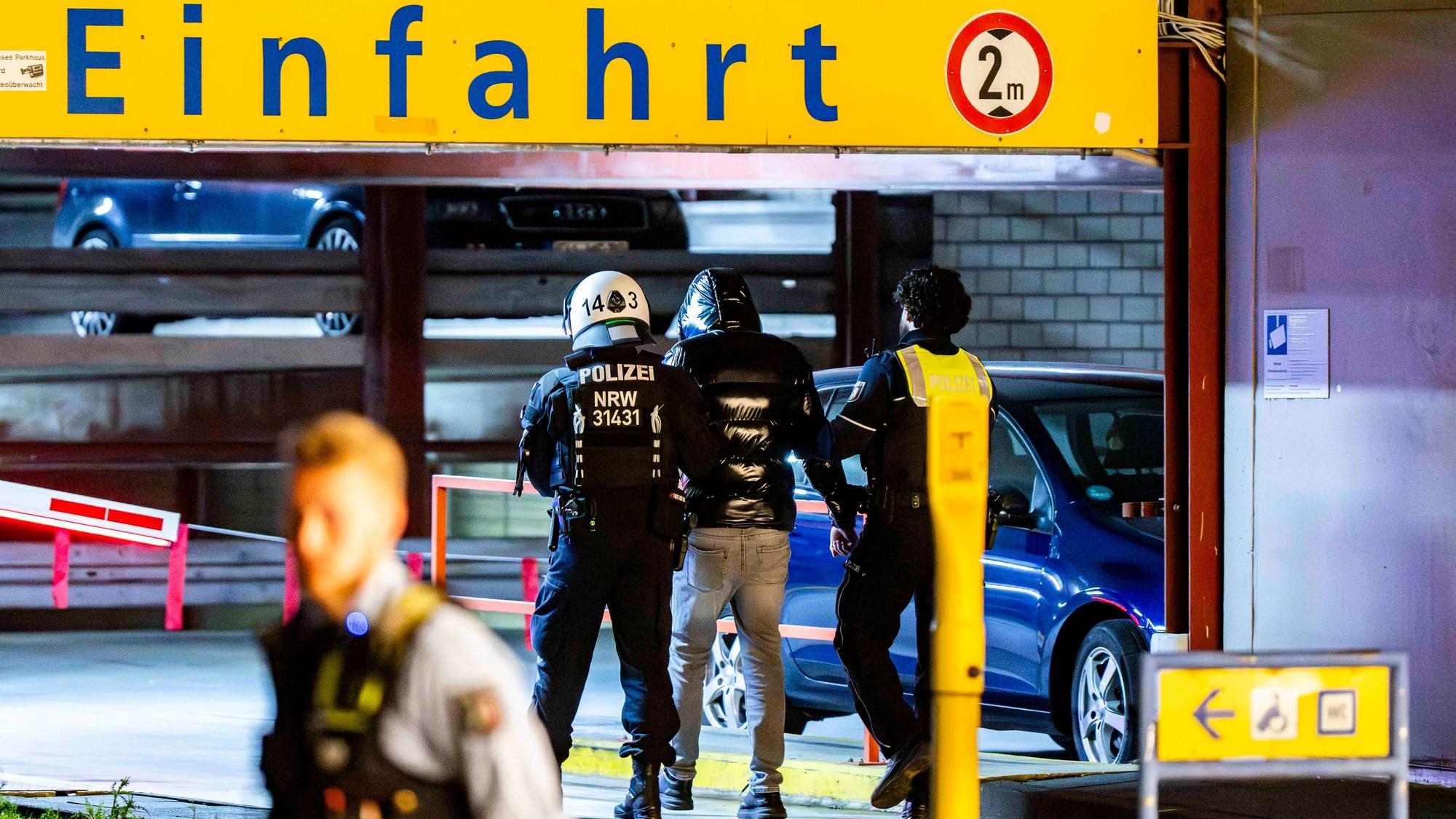 Das Bild zeigt zwei Polizisten, die einen Mann in ein Parkhaus führen.