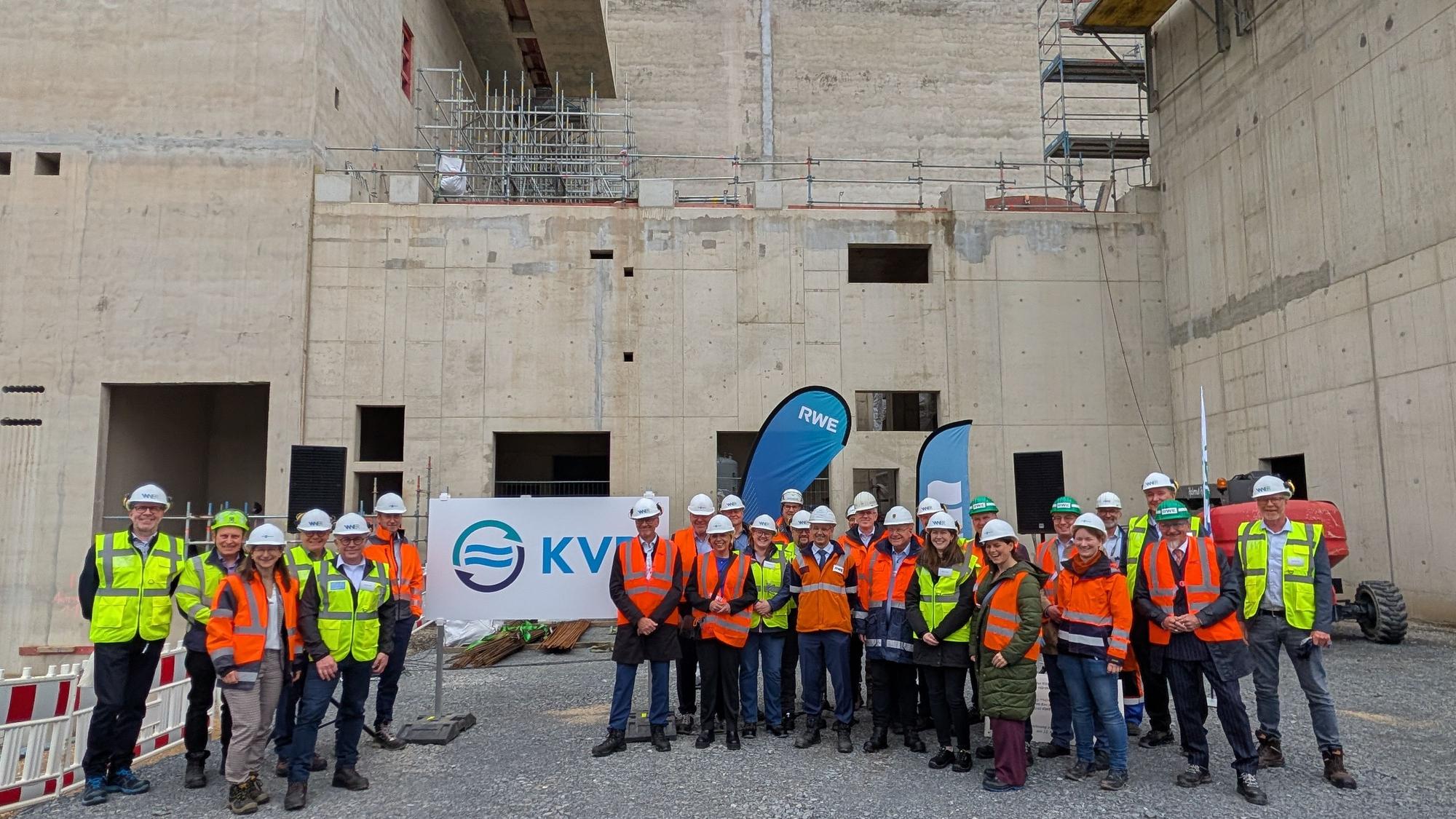 Das Foto zeigt eine große Gruppe von Menschen in Warnwesten und mit Schutzhelmen vor dem Rohbau.