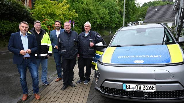 Fünf Männer stehen nebeneinander und neben einem Ordnungsamt-Wagen.