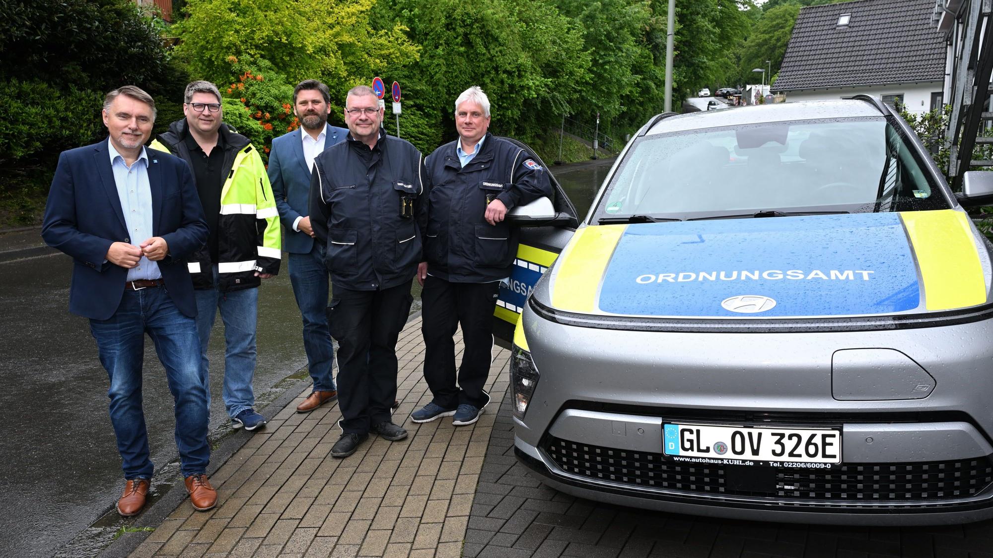 Fünf Männer stehen nebeneinander und neben einem Ordnungsamt-Wagen.