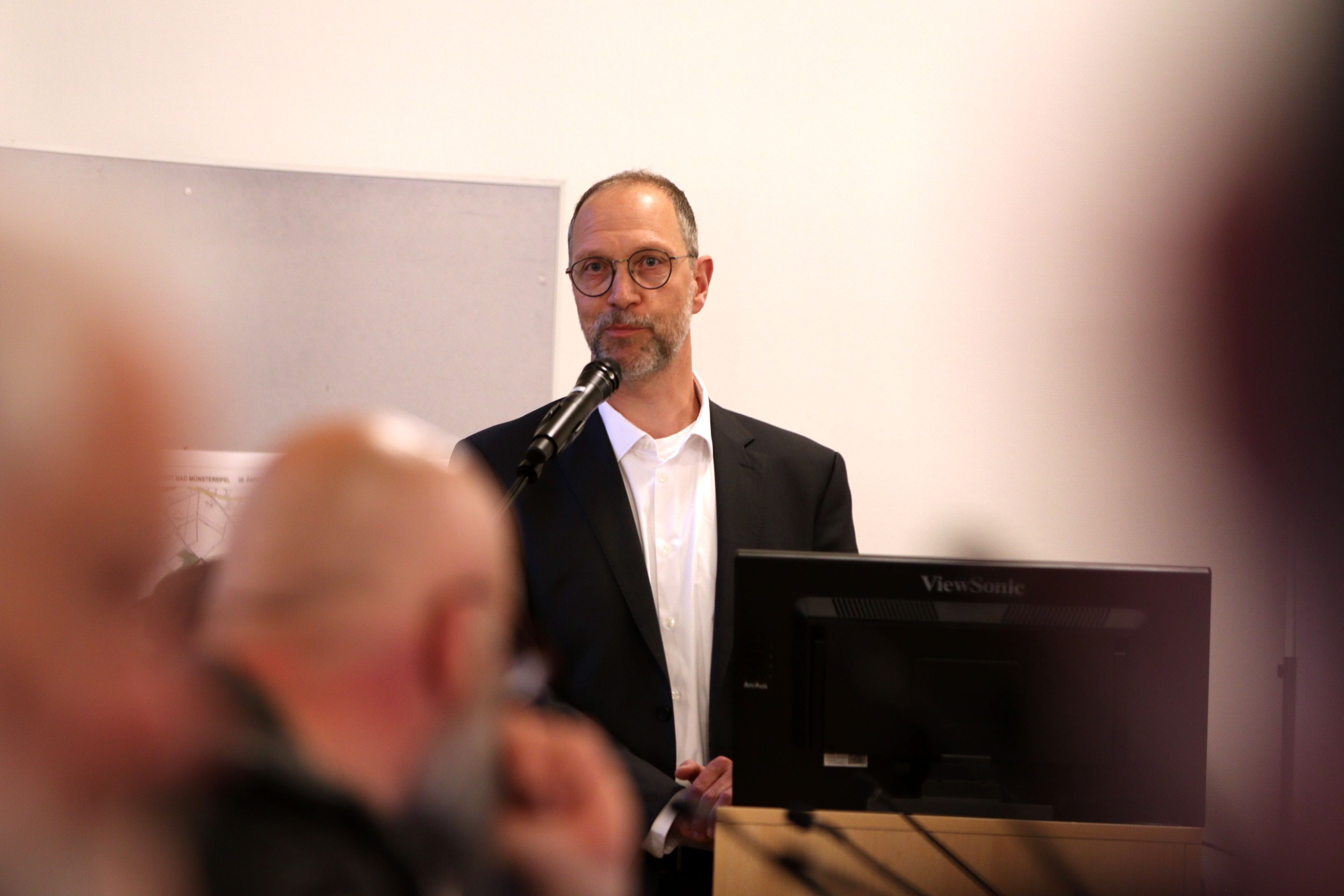 Wolfgang Greuel stellt sich dem Stadtratin Bad Münstereifel vor und steht an einem Mikrofon.