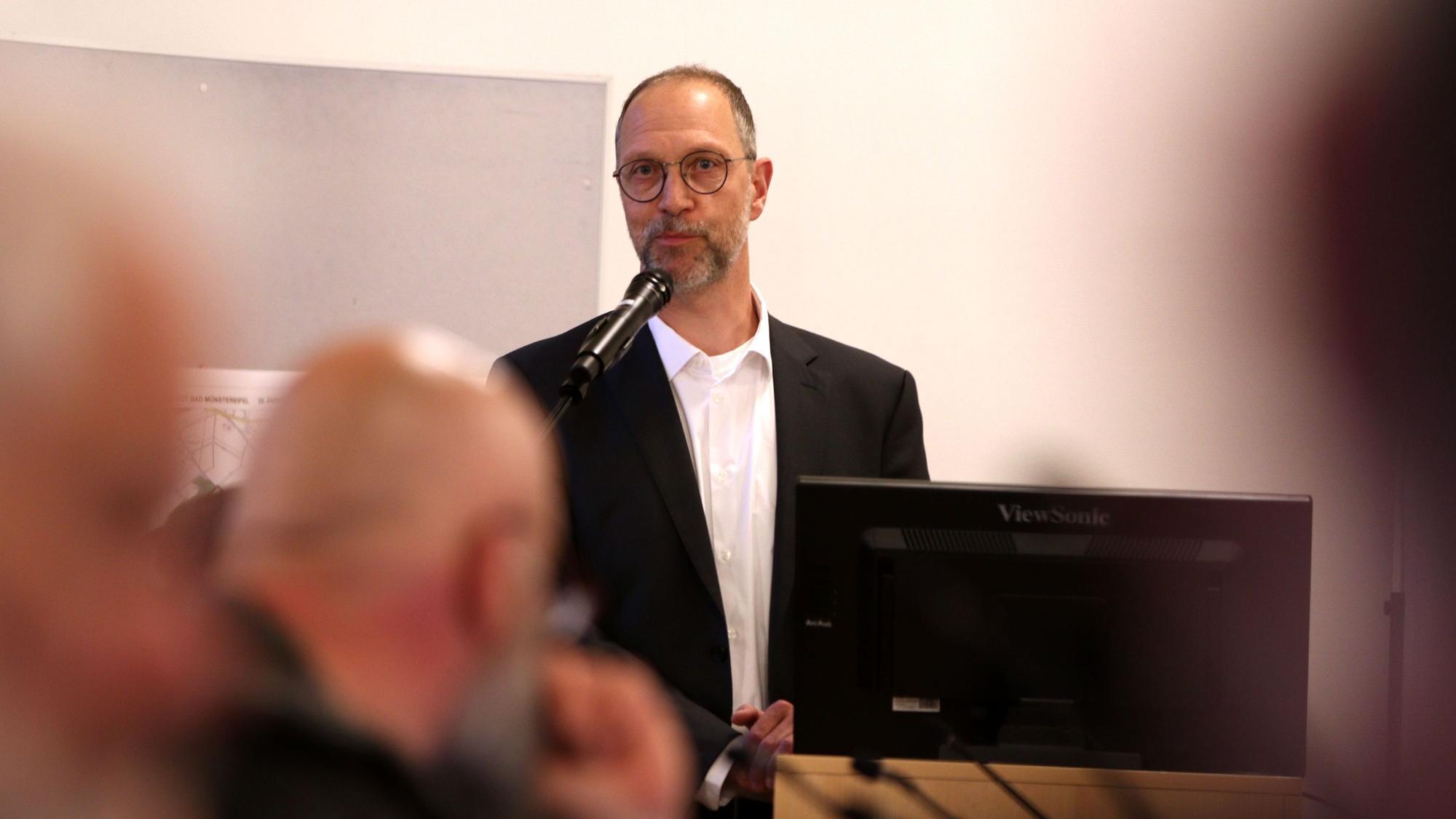 Wolfgang Greuel stellt sich dem Stadtratin Bad Münstereifel vor und steht an einem Mikrofon.