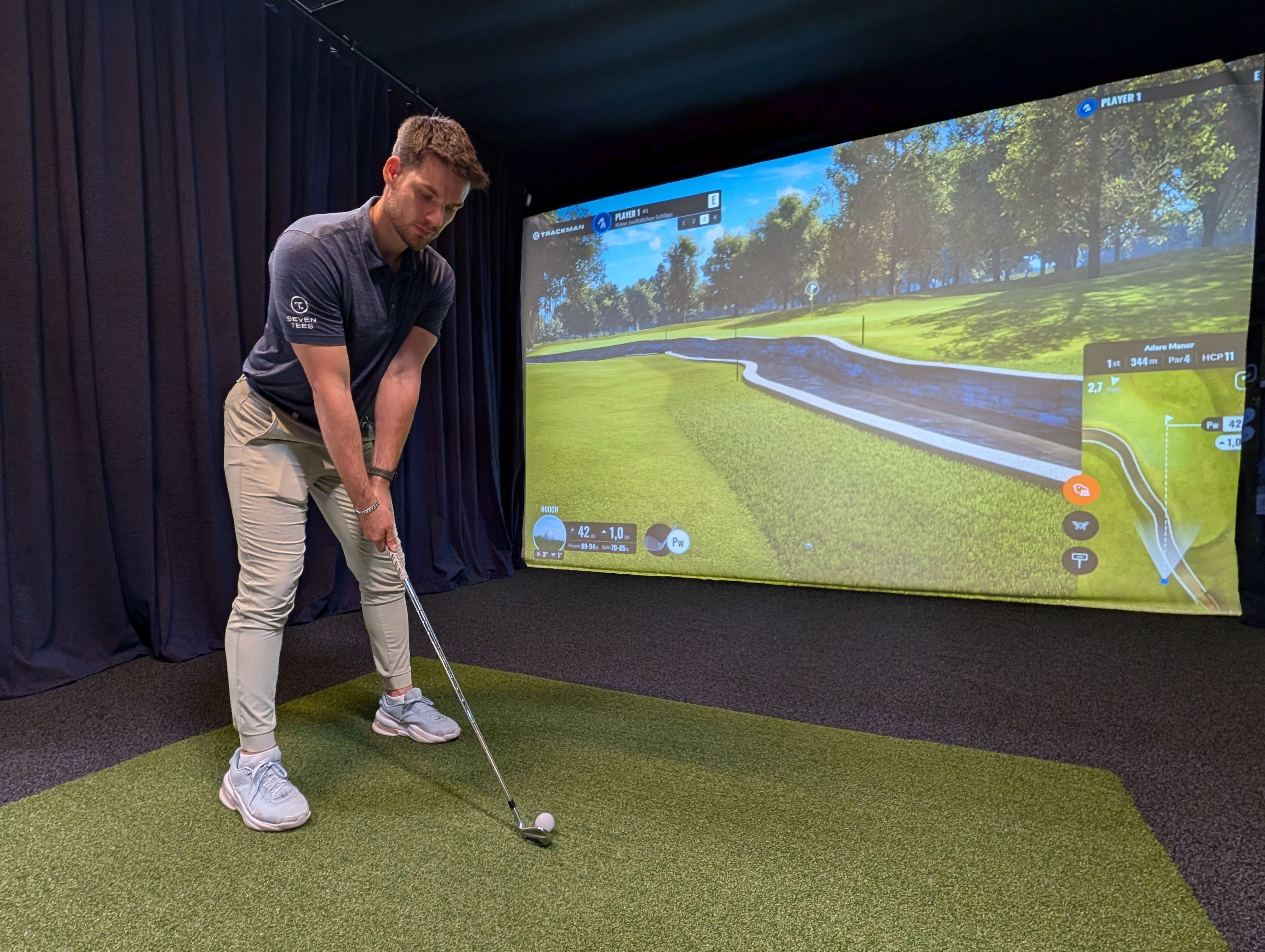 Das Foto zeigt den Inhaber mit Golfschläger am Abschlag vor der Videowand.