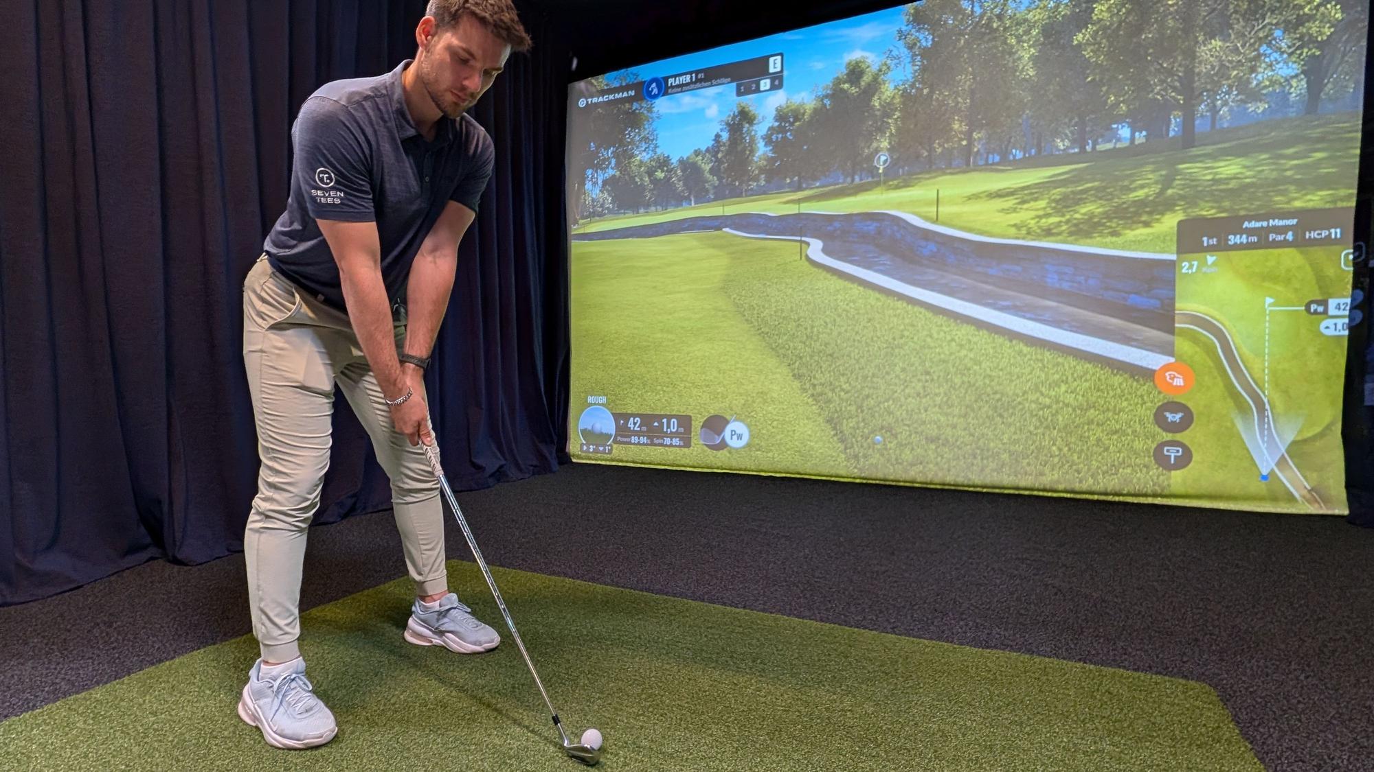 Das Foto zeigt den Inhaber mit Golfschläger am Abschlag vor der Videowand.