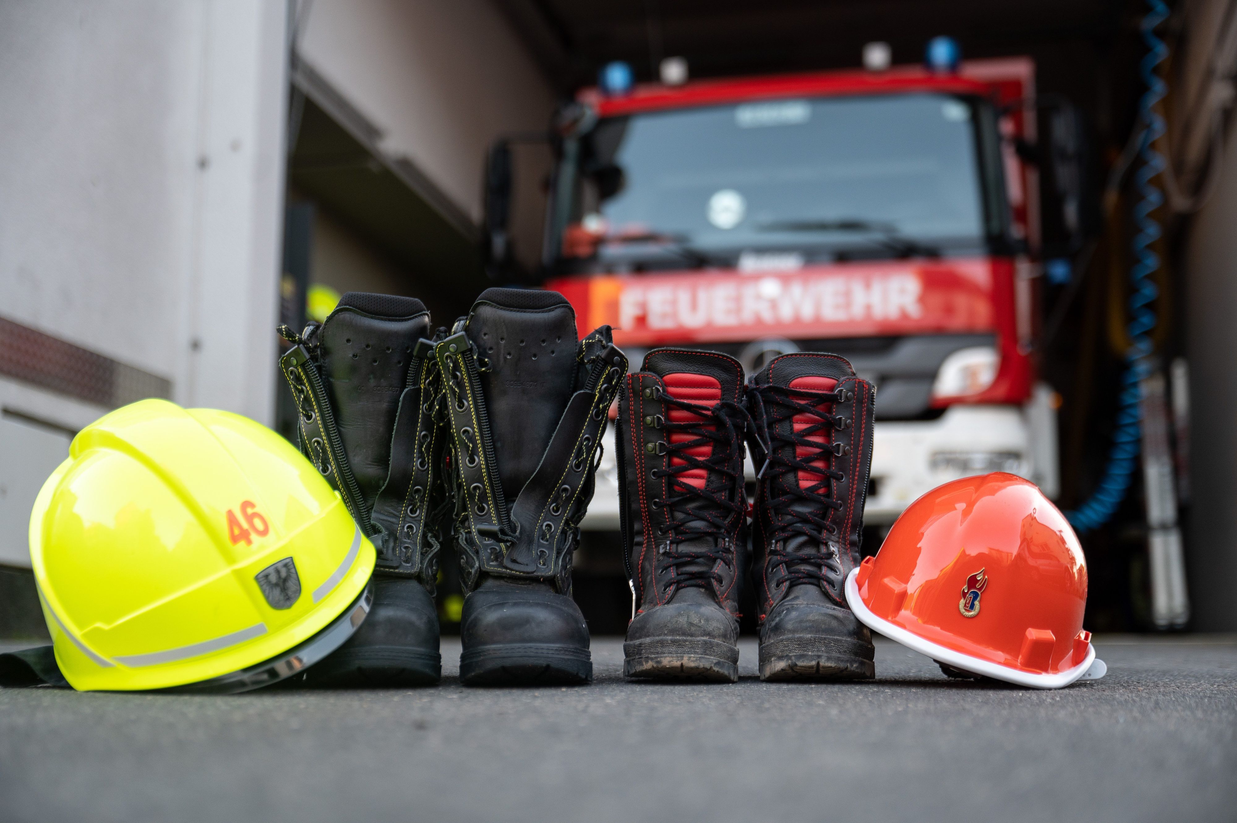 Stiefel und Helm eines Mitglieds der Jugendfeuerwehr und einem erwachsenen Mitglied der Freiwilligen Feuerwehr Frankfurt-Seckbach stehen vor einem Feuerwehrhaus.