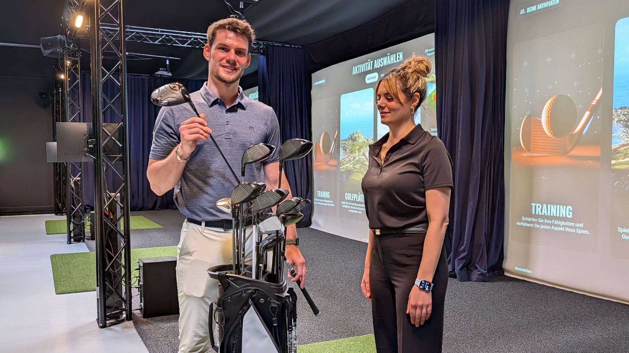 Das Foto zeigt das Inhaberpaar mit Golfausrüstung in der Golfhalle.