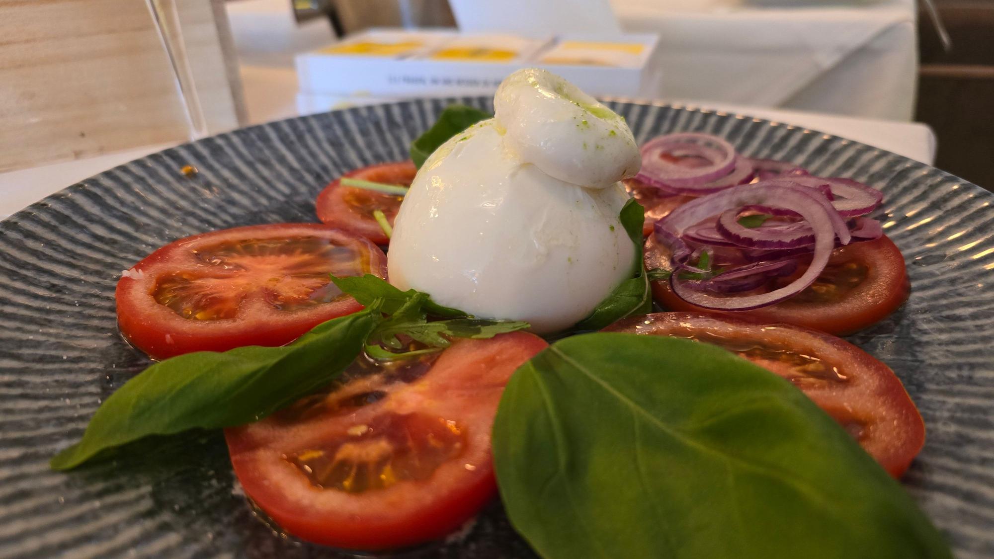 Tellergericht mit Tomatenscheiben, Burrata und Basilikum ist zu sehen