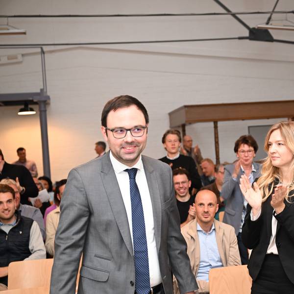 Ein Mann lächelt, mehrere Menschen applaudieren.