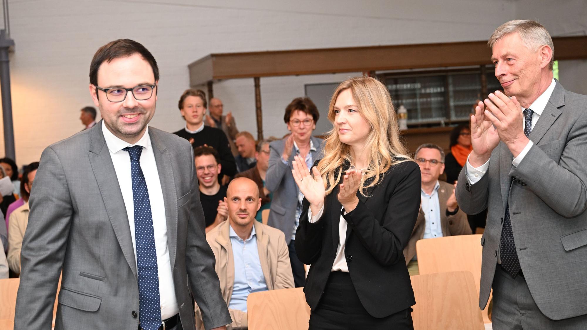 Ein Mann lächelt, mehrere Menschen applaudieren.