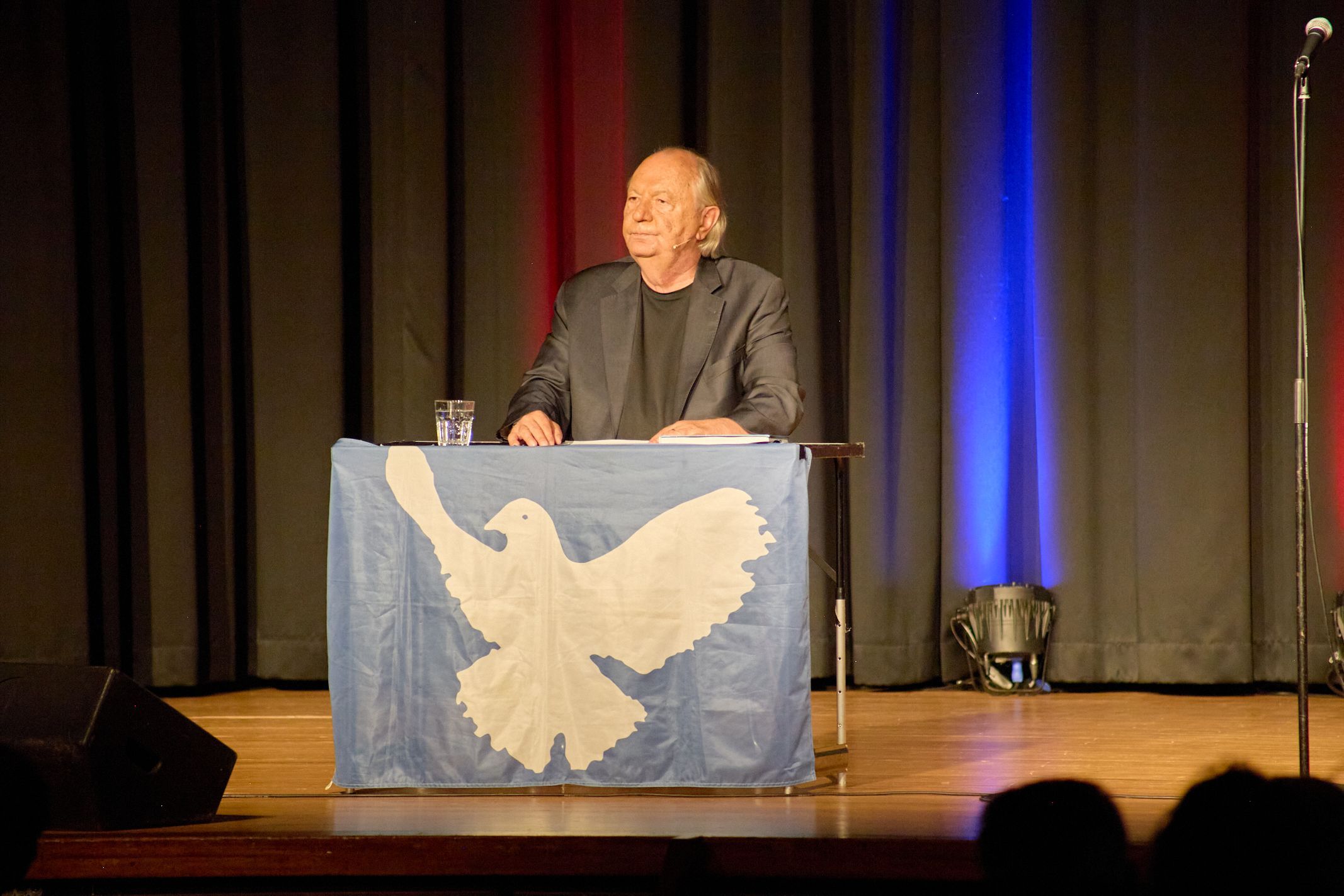 Wilfried Schmickler steht hinter einem Pult, das mit einer Friedenstaube geschmückt ist.