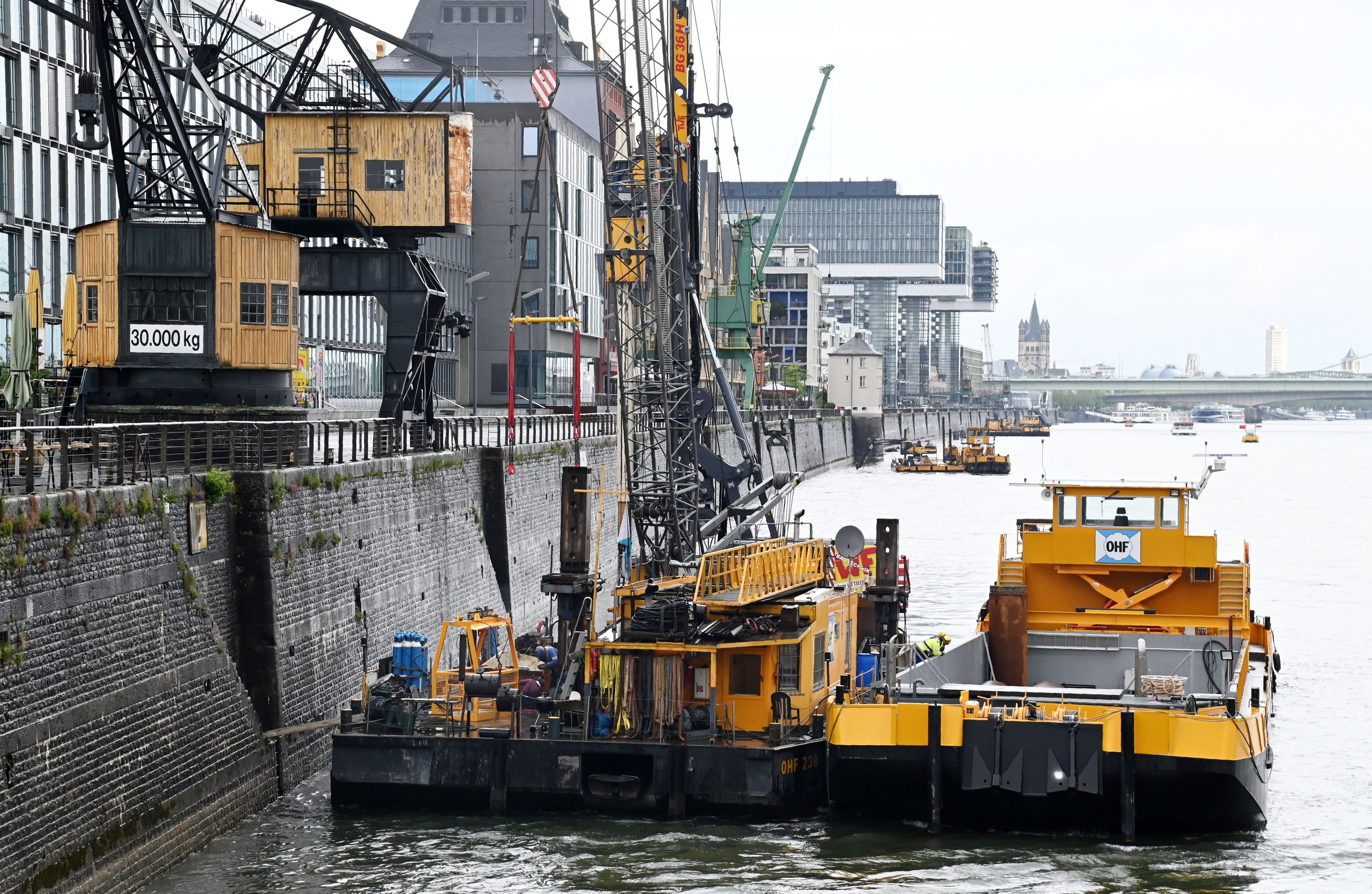 Am Rheinufer vor dem Rheinauhafen liegen Schiffe einer Wasserbaufirma vor der Kaimauer vor Anker und führen Arbeiten durch.