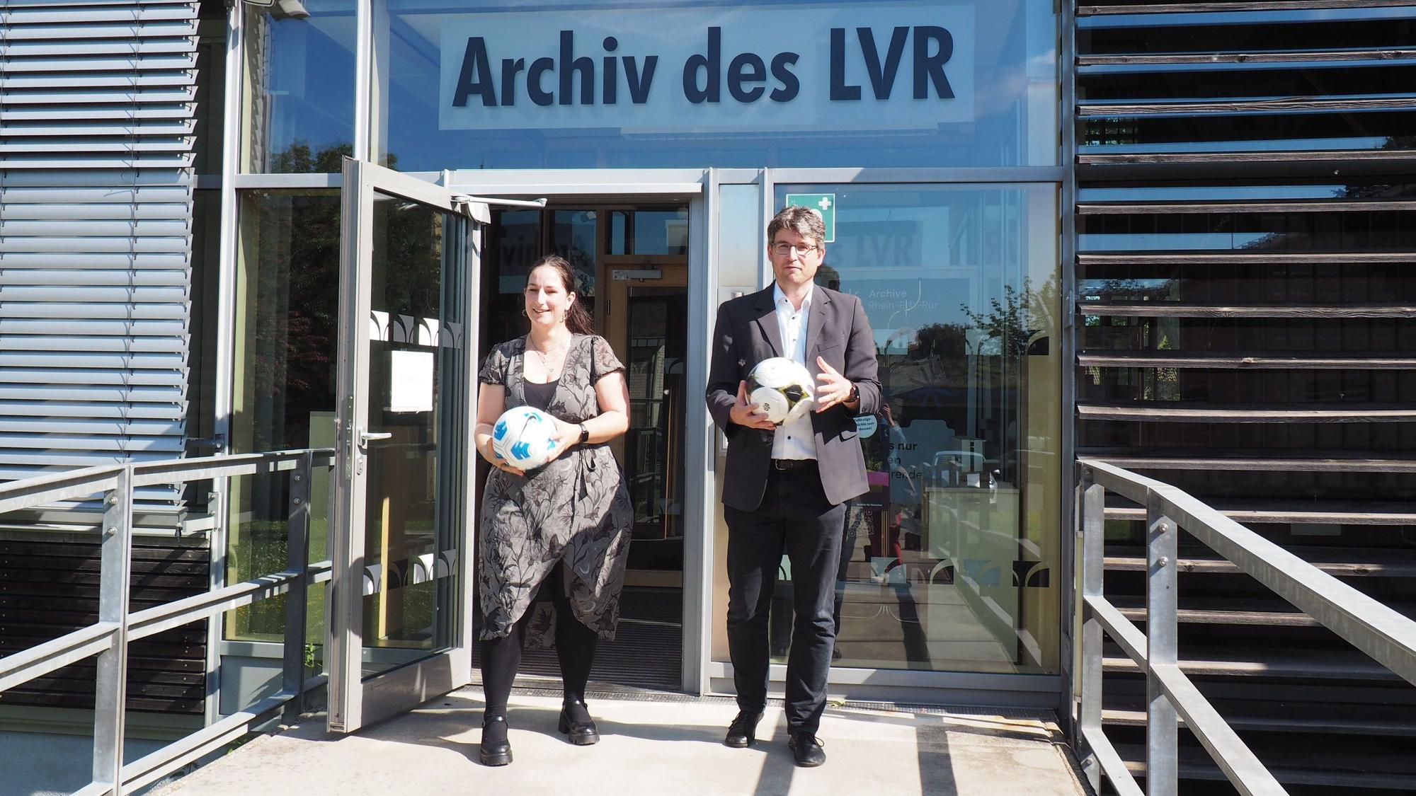 das Foto zeigt eine Frau und einen Mann mit Bällen in den Händen, die aus der Tür des LVR-Archivs kommen.