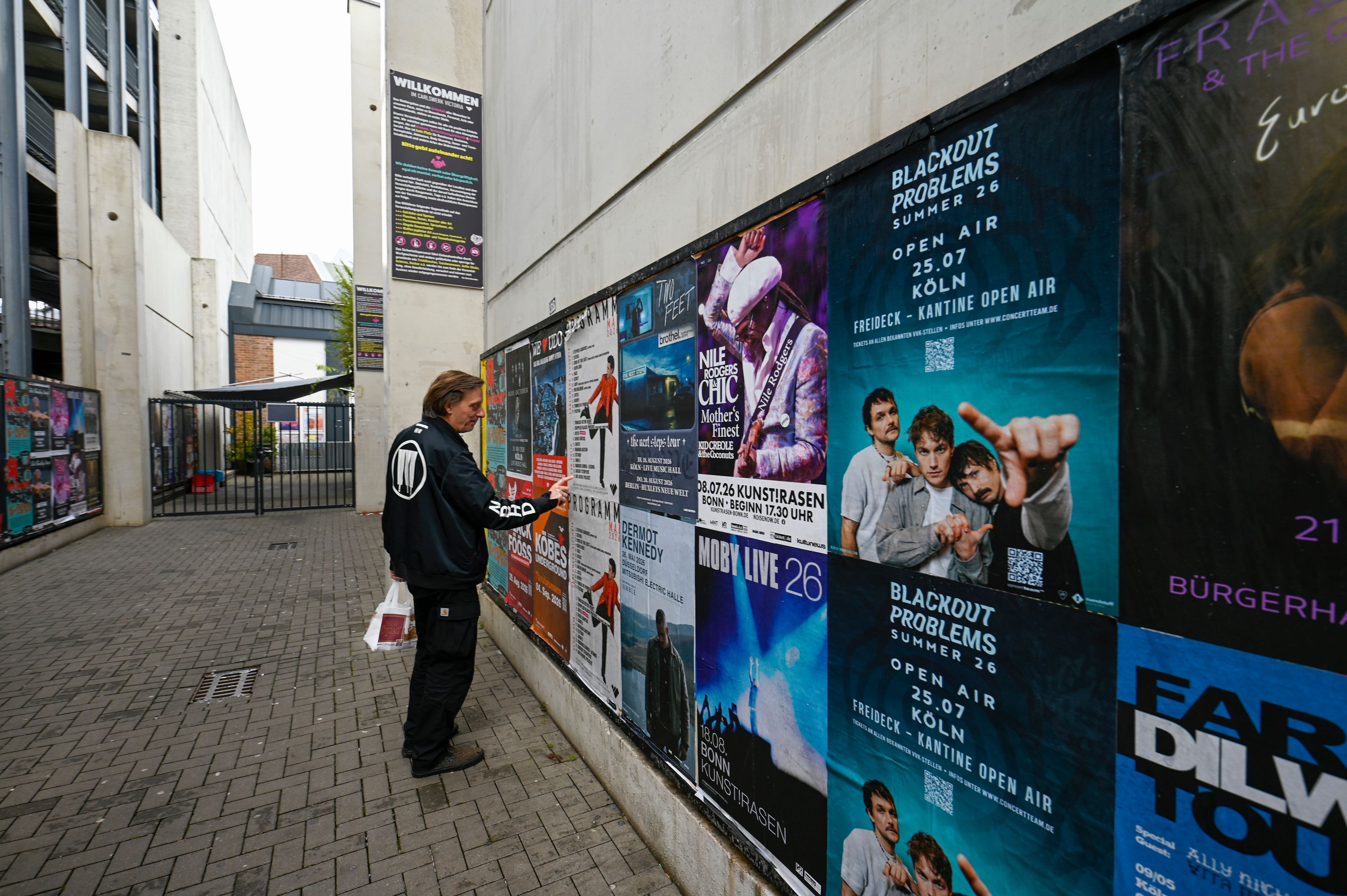 Ein Mann steht vor einer Wand mit Konzert-Plakaten.