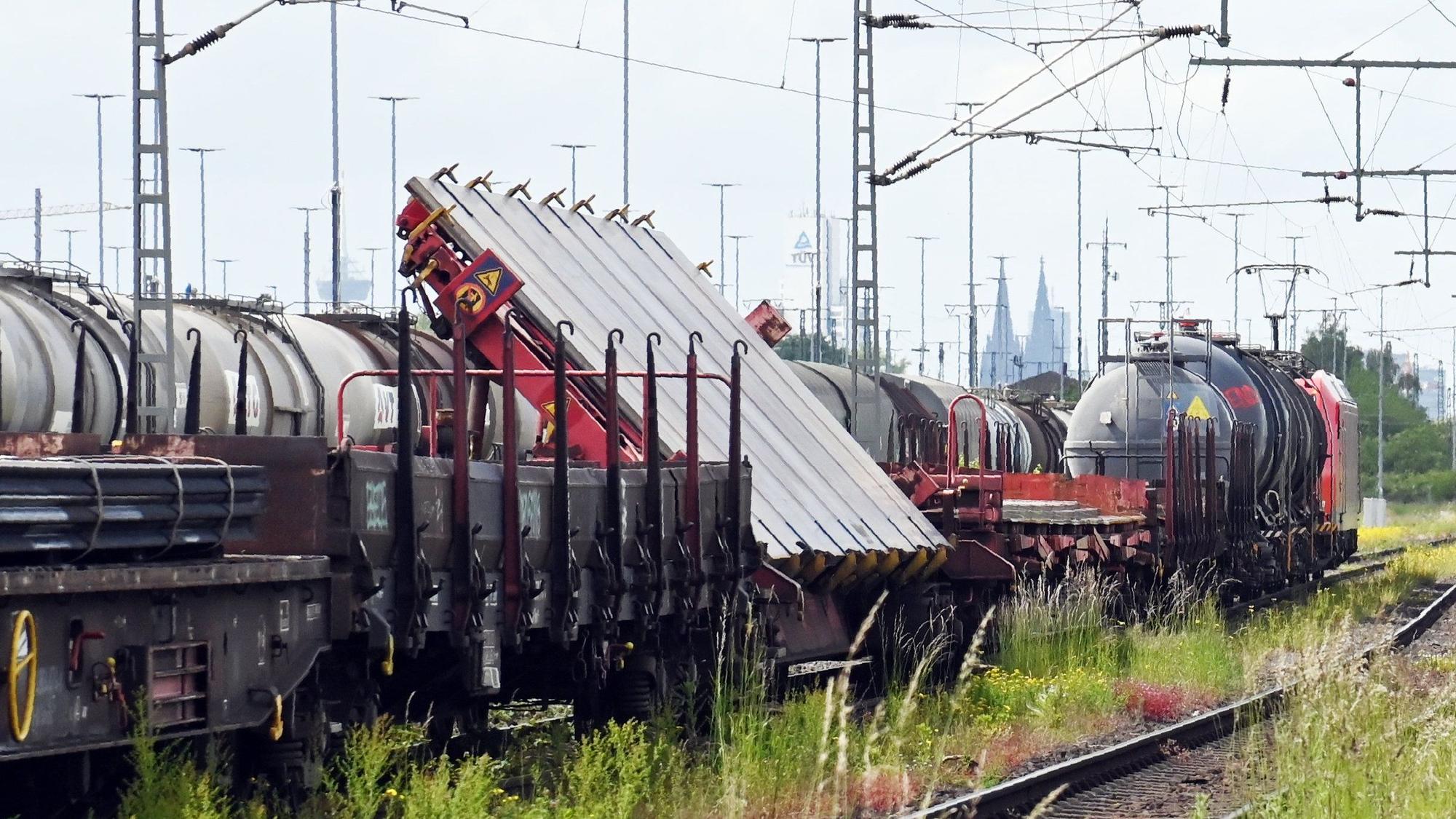 Mehrere Güterwagen in einer Reihung, einer ist mit einer sehr großen Stahlplatte beladen, die schräg auf dem Waggon befestigt ist.