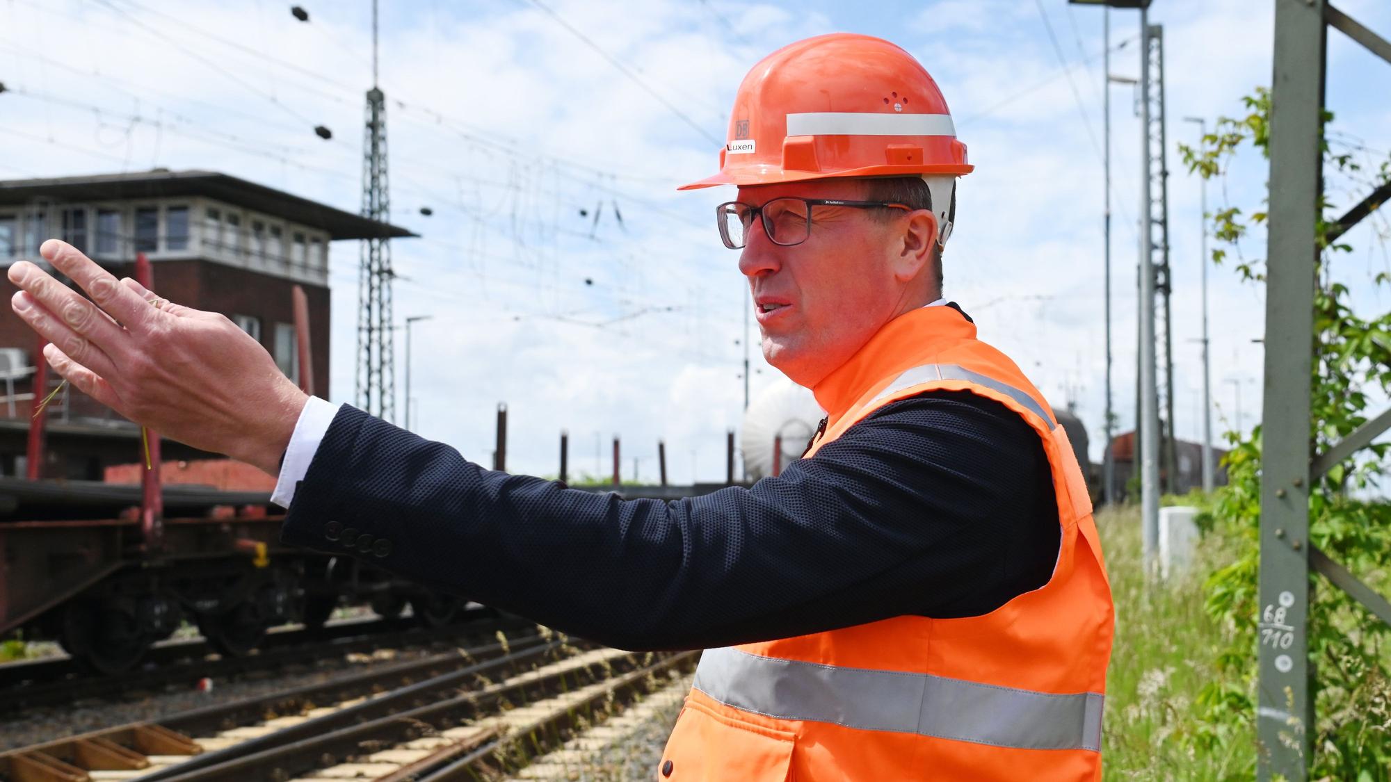 Herr Luxen steht an den Gleisen in orangefarbener Weste und mit Schutzhelm und erklärt etwas.