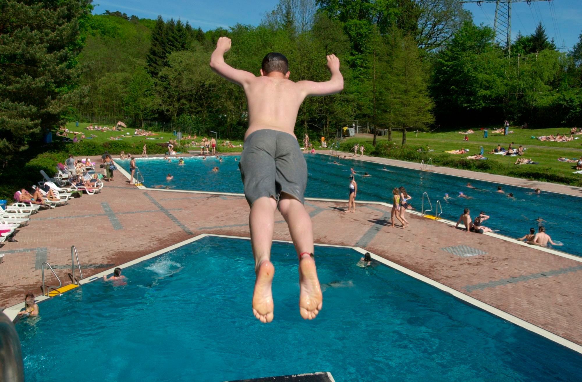Ein junger Mann springt von einem Springturm in das Wasserbecken im Freibad Milchborntal.