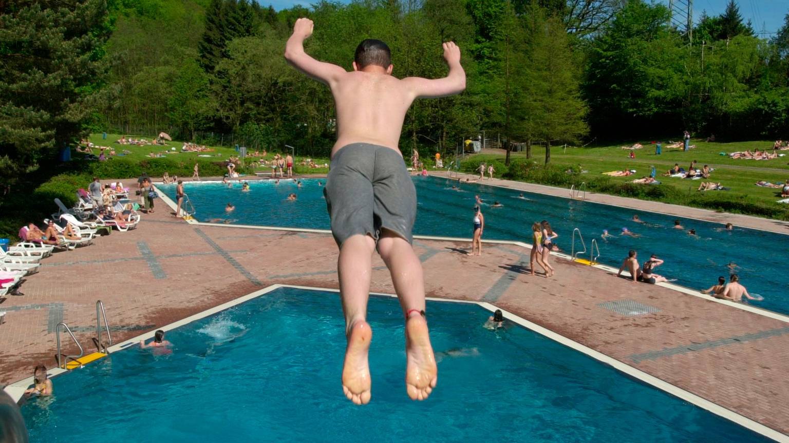 Ein junger Mann springt von einem Springturm in das Wasserbecken im Freibad Milchborntal.