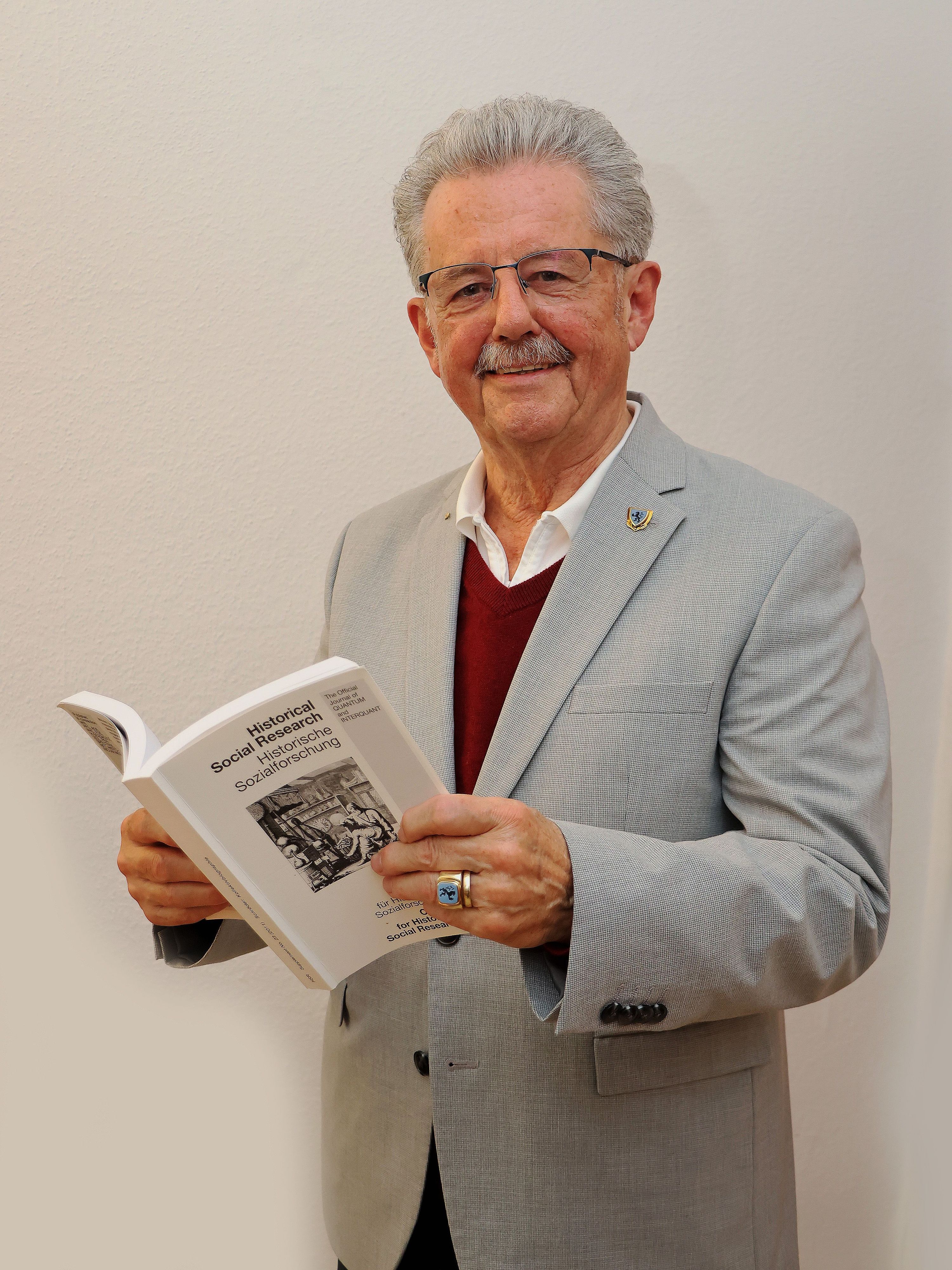 Ein Mann in grauem Sakko steht vor einer weißen Wand.