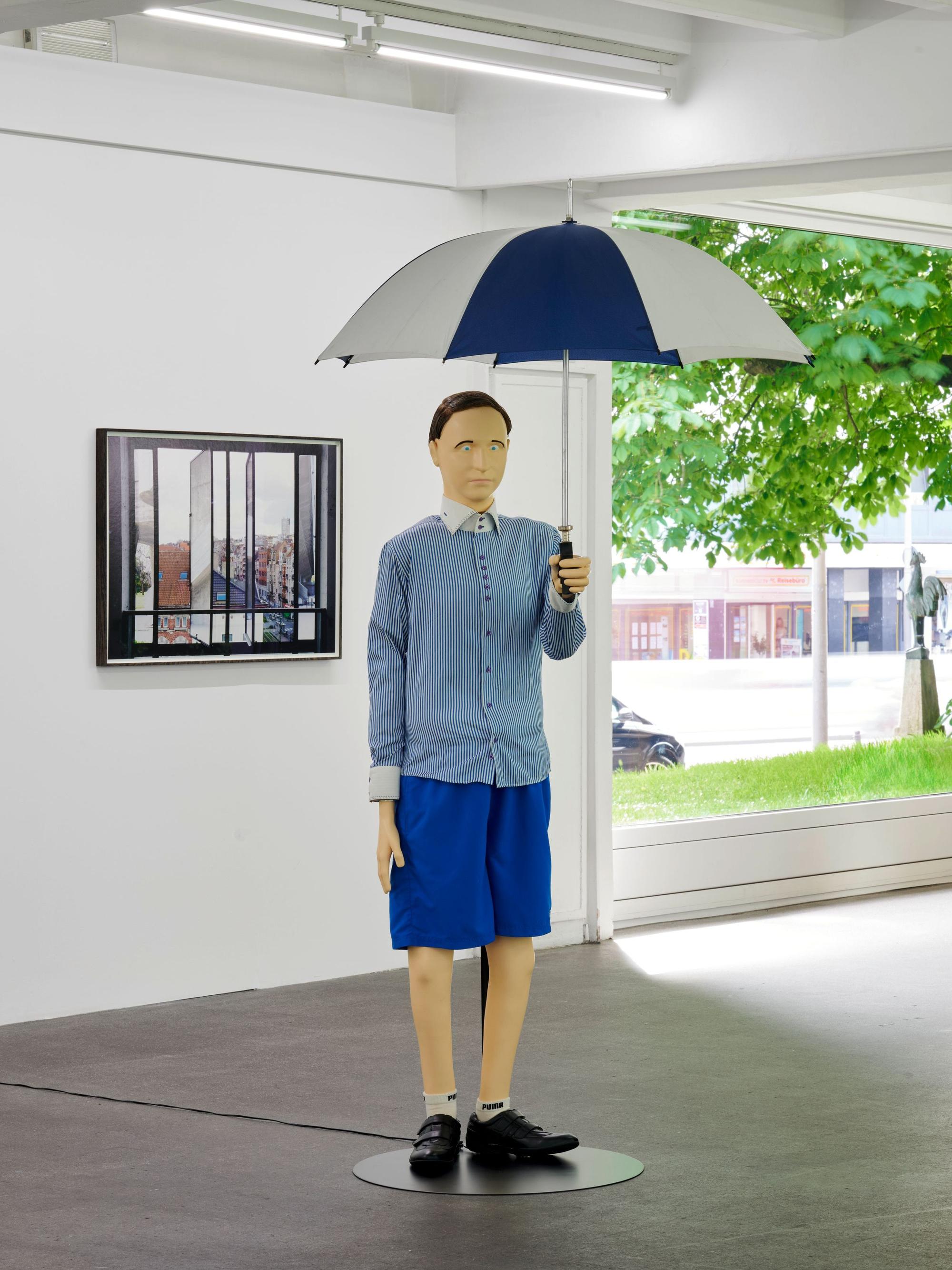 Eine lebensgroße Puppe hält einen Regenschirm in der Hand.
