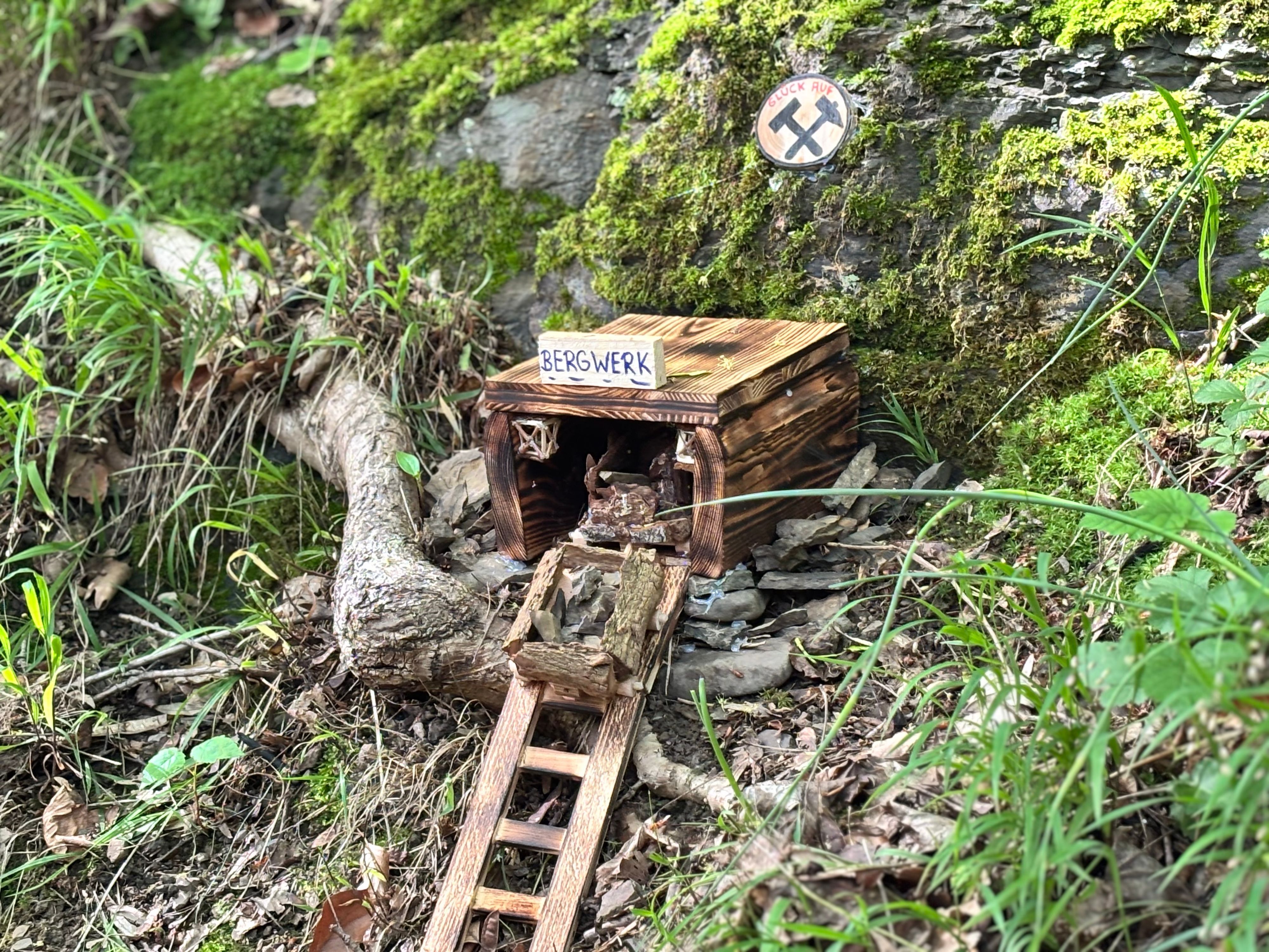Ein Miniaturbergwerk steht am Wegesrand eines Waldes bei Felsen.