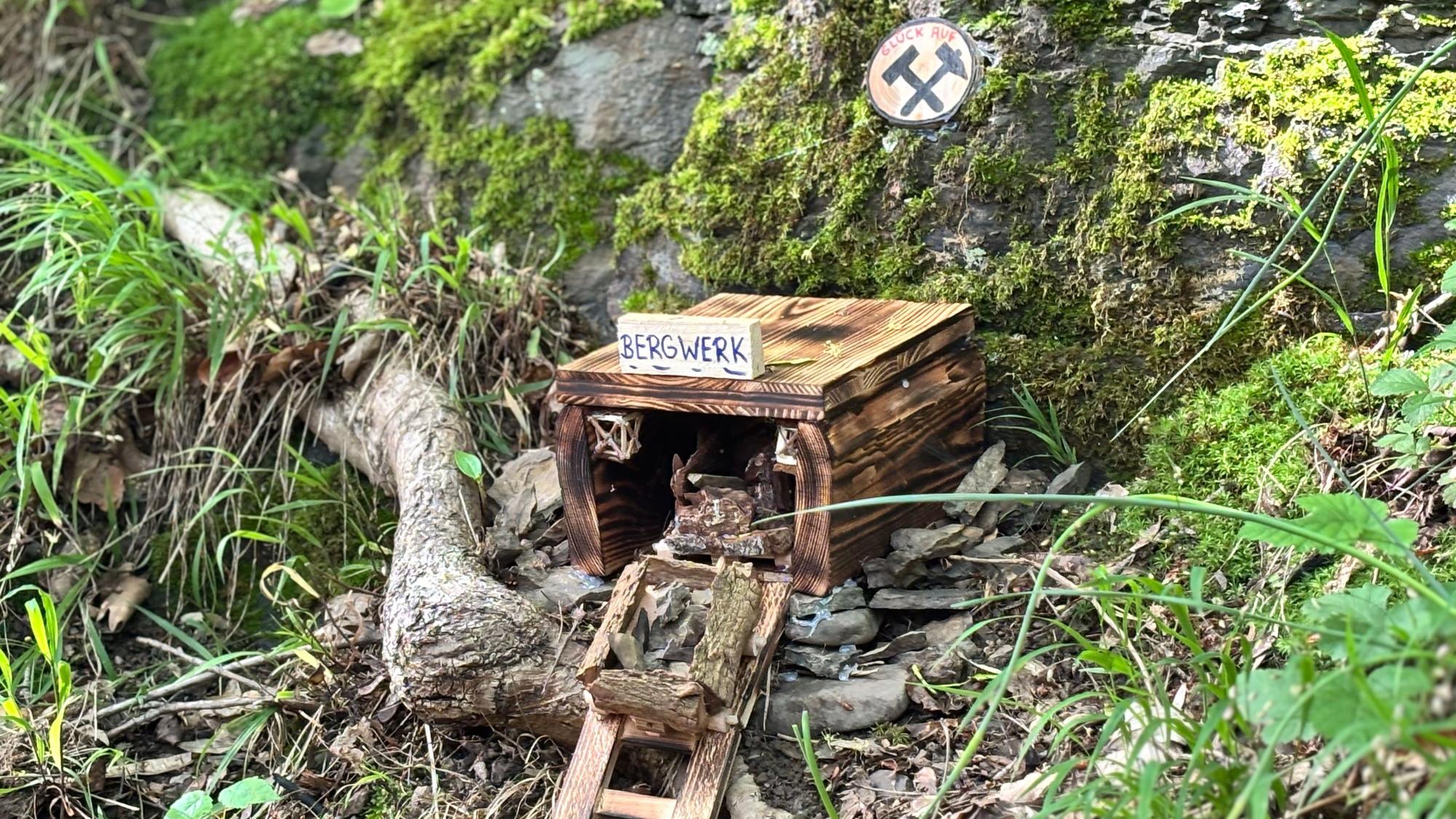 Ein Miniaturbergwerk steht am Wegesrand eines Waldes bei Felsen.