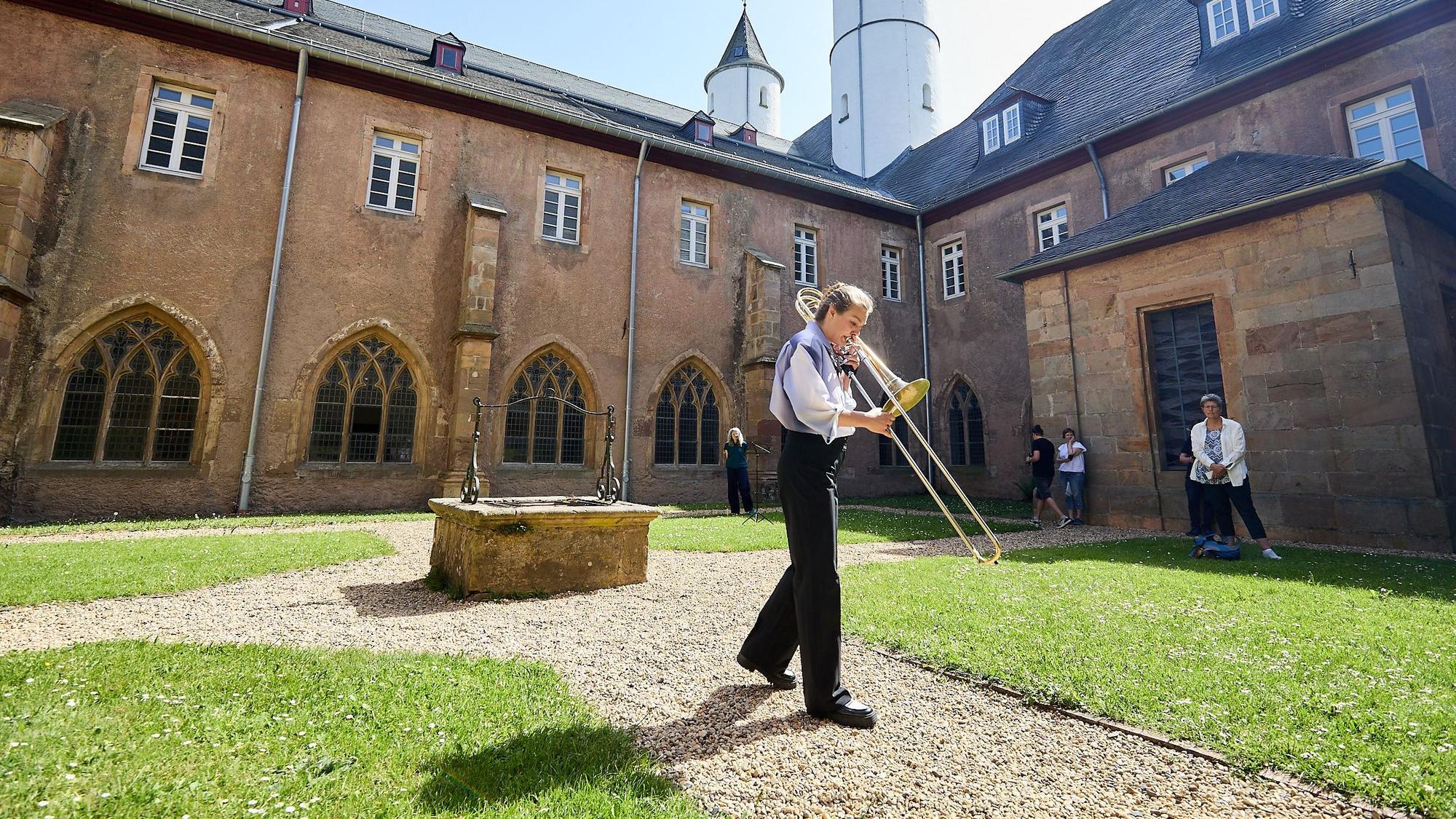 Maxine Troglauer steht bei Sonnenschein in einem Innenhof des Klosters in Steinfeld und spielt Posaune.