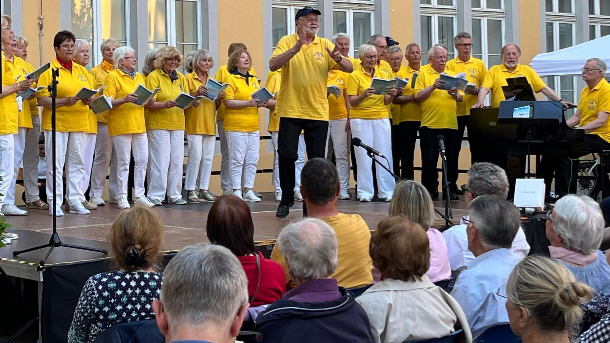 Zu sehen ist ein Chor beim Auftritt auf einer Bühne.