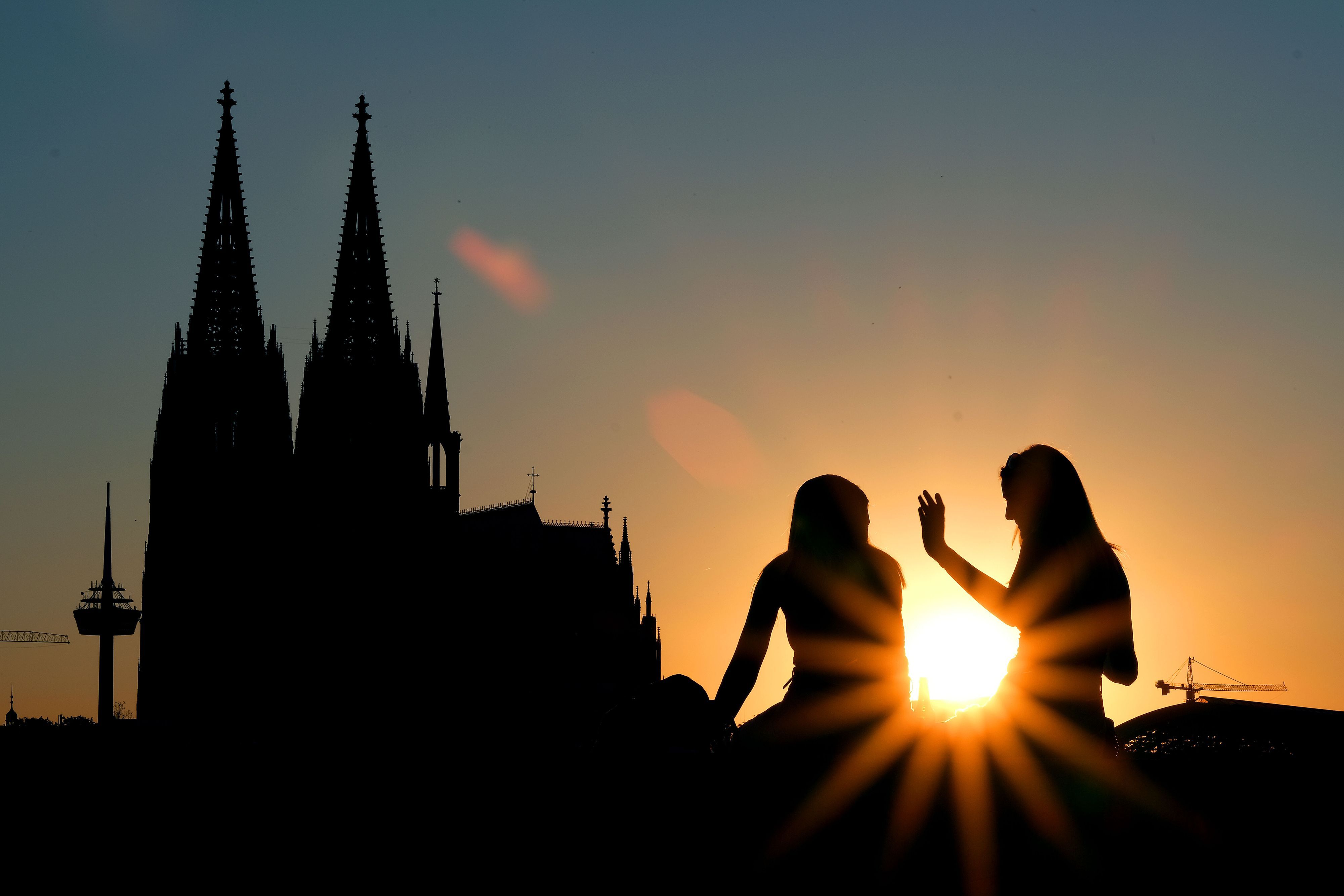 Zwei Frauen sitzen im Sonnenuntergang am Rheinboulevard vor dem Dom. (Archivbild)