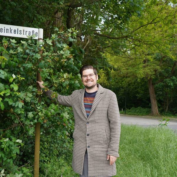 Das Foto zeigt einen Mann vor einem Straßenschild.