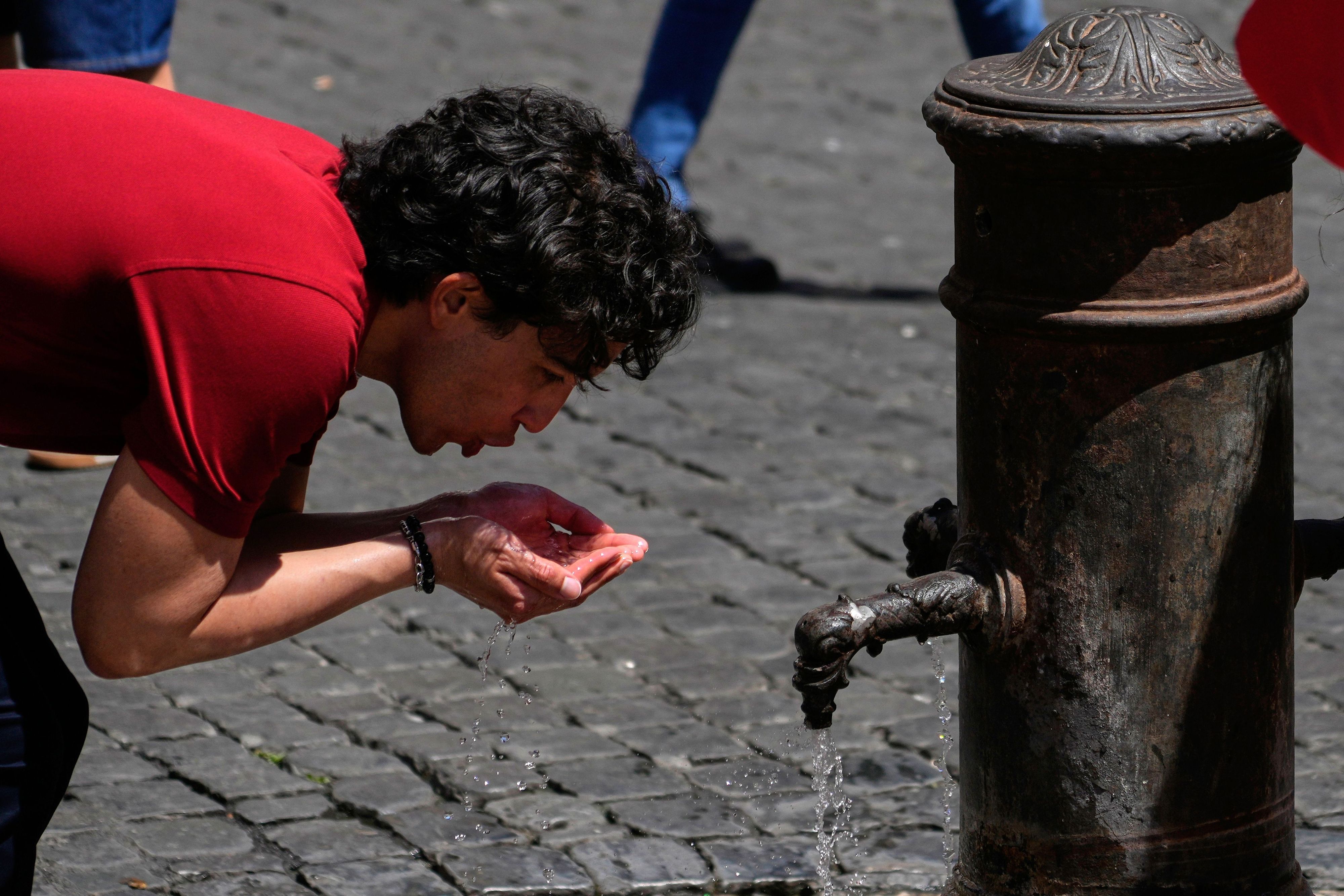 Italien, Rom: Ein Mann trinkt Wasser an einem Brunnen in der Innenstadt, während die Temperaturen auf mehr als 30 Grad Celsius steigen.