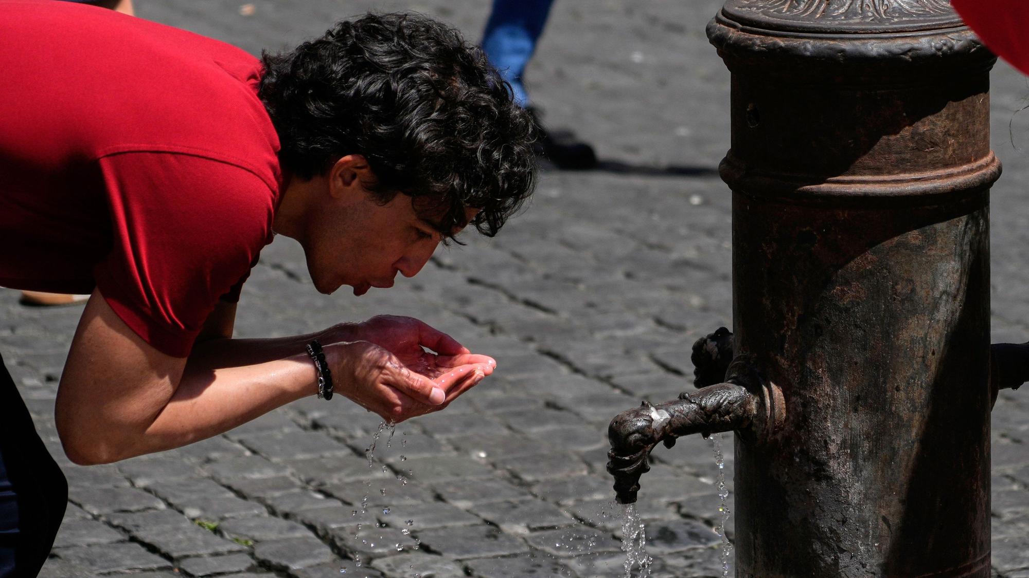 Italien, Rom: Ein Mann trinkt Wasser an einem Brunnen in der Innenstadt, während die Temperaturen auf mehr als 30 Grad Celsius steigen.
