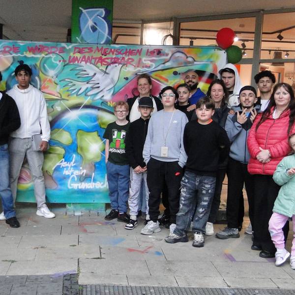 Ein großflächiges Graffiti und darum versammelte Menschen verschiedenen Alters