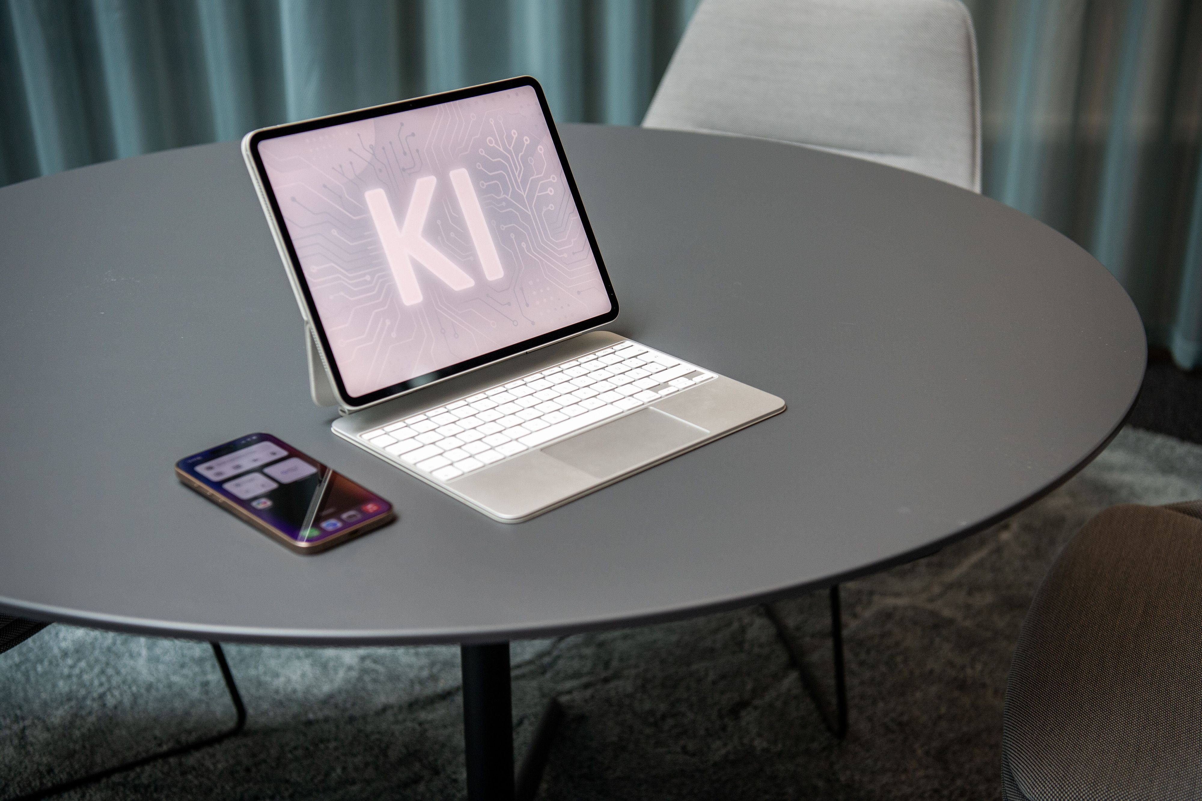 Ein Computer steht auf einem Tisch, daneben ein Handy. Auf dem Computerbildschirm ist „KI “zu lesen. (Symbolbild)