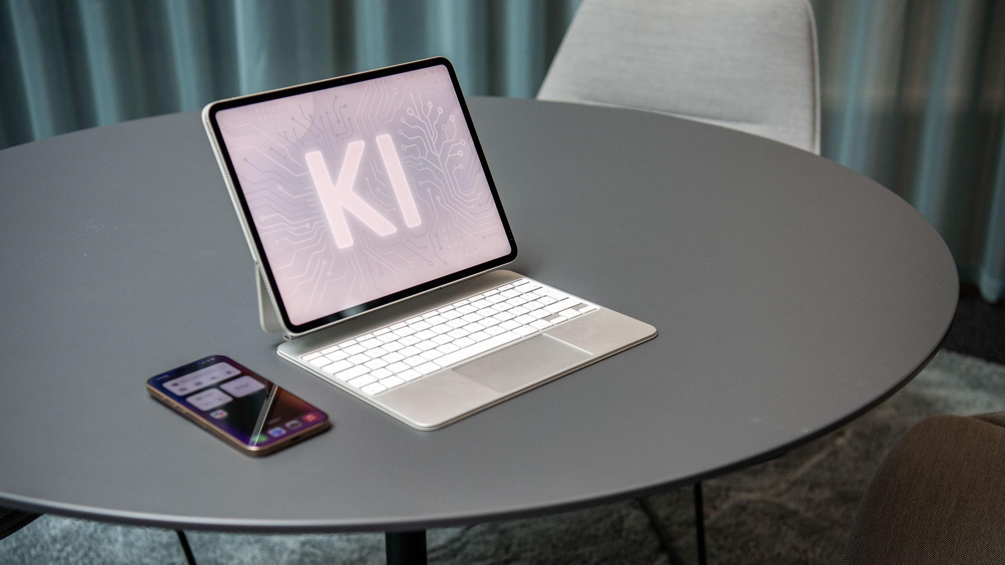Ein Computer steht auf einem Tisch, daneben ein Handy. Auf dem Computerbildschirm ist „KI “zu lesen. (Symbolbild)