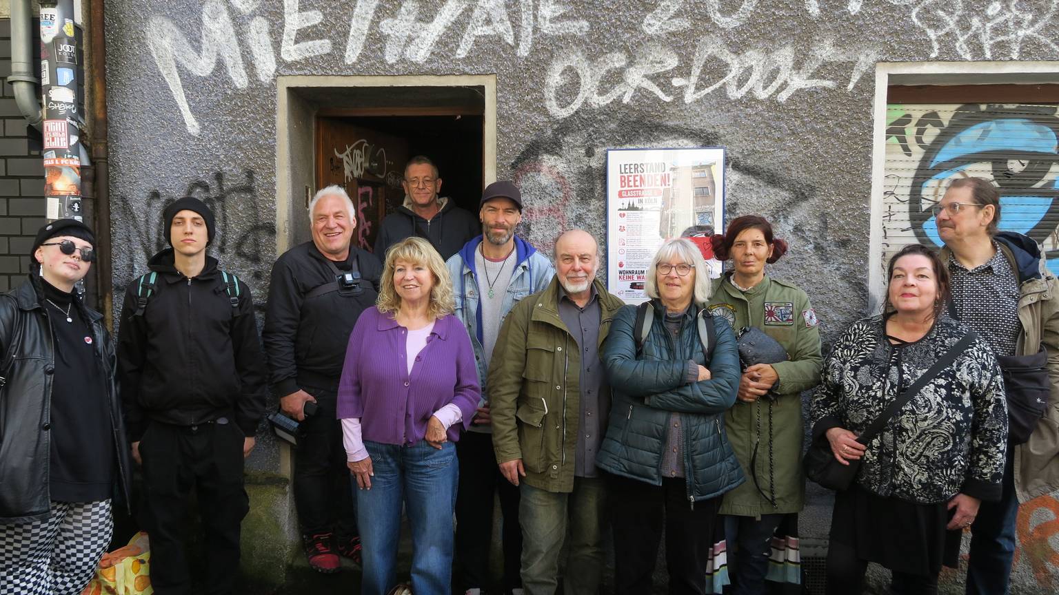 Eine Gruppe Menschen steht vor einem Haus mit beschmierter Fassade.