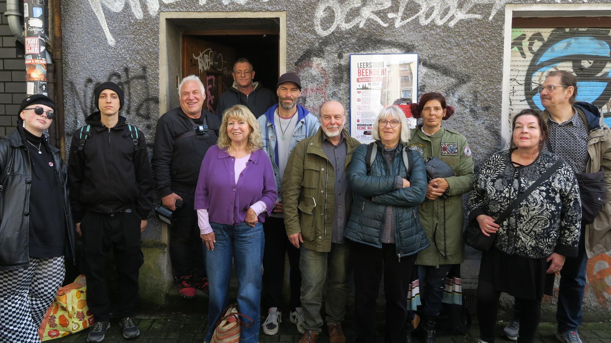 Eine Gruppe Menschen steht vor einem Haus mit beschmierter Fassade.
