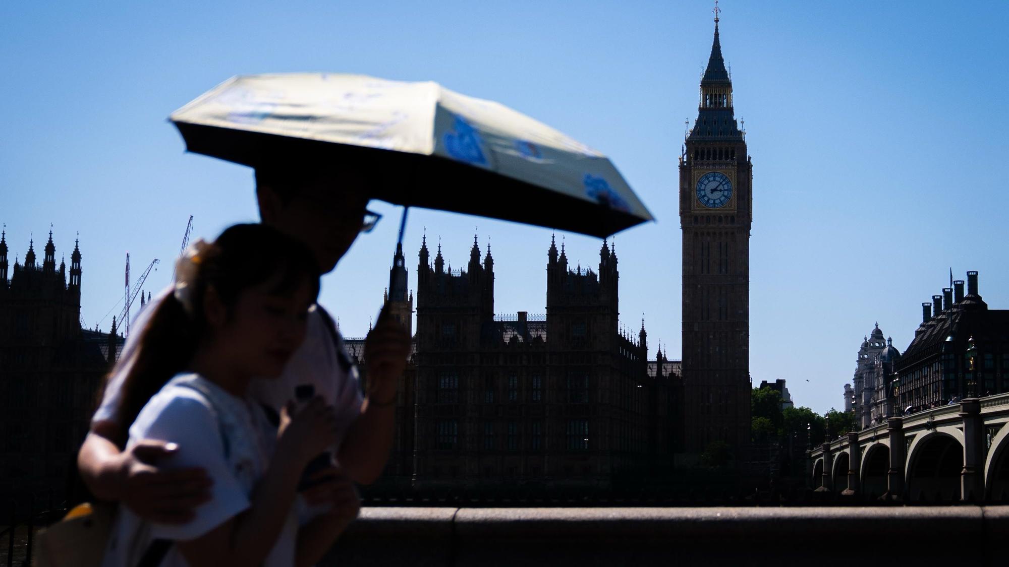 Touristen schützen sich vor dem heißen Wetter unter einem Regenschirm auf der Westminster Bridge im Zentrum Londons.