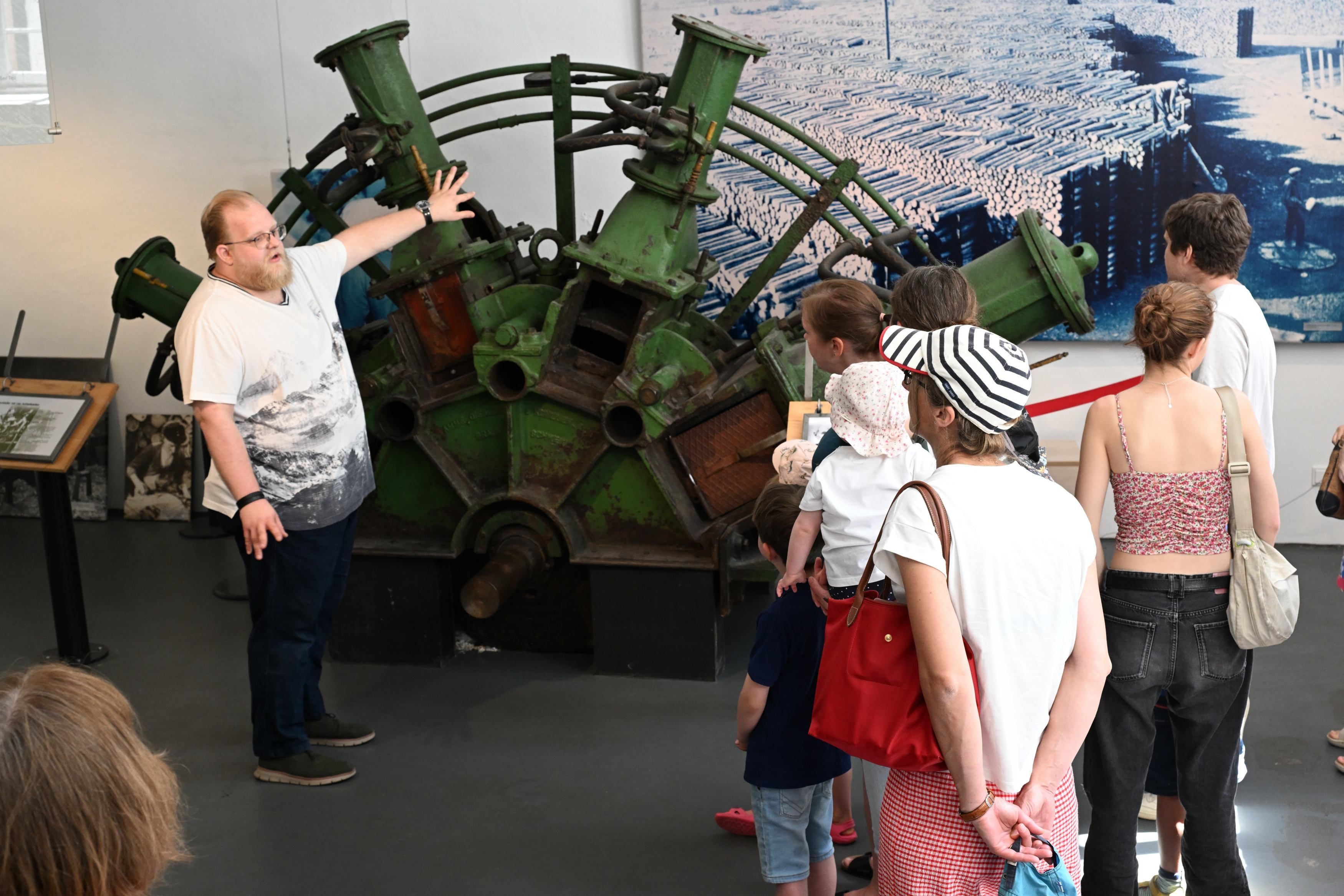Zu sehen ist ein Museumsguide vor einer Gruppe, wie er über ein Ausstellungsstück spricht.