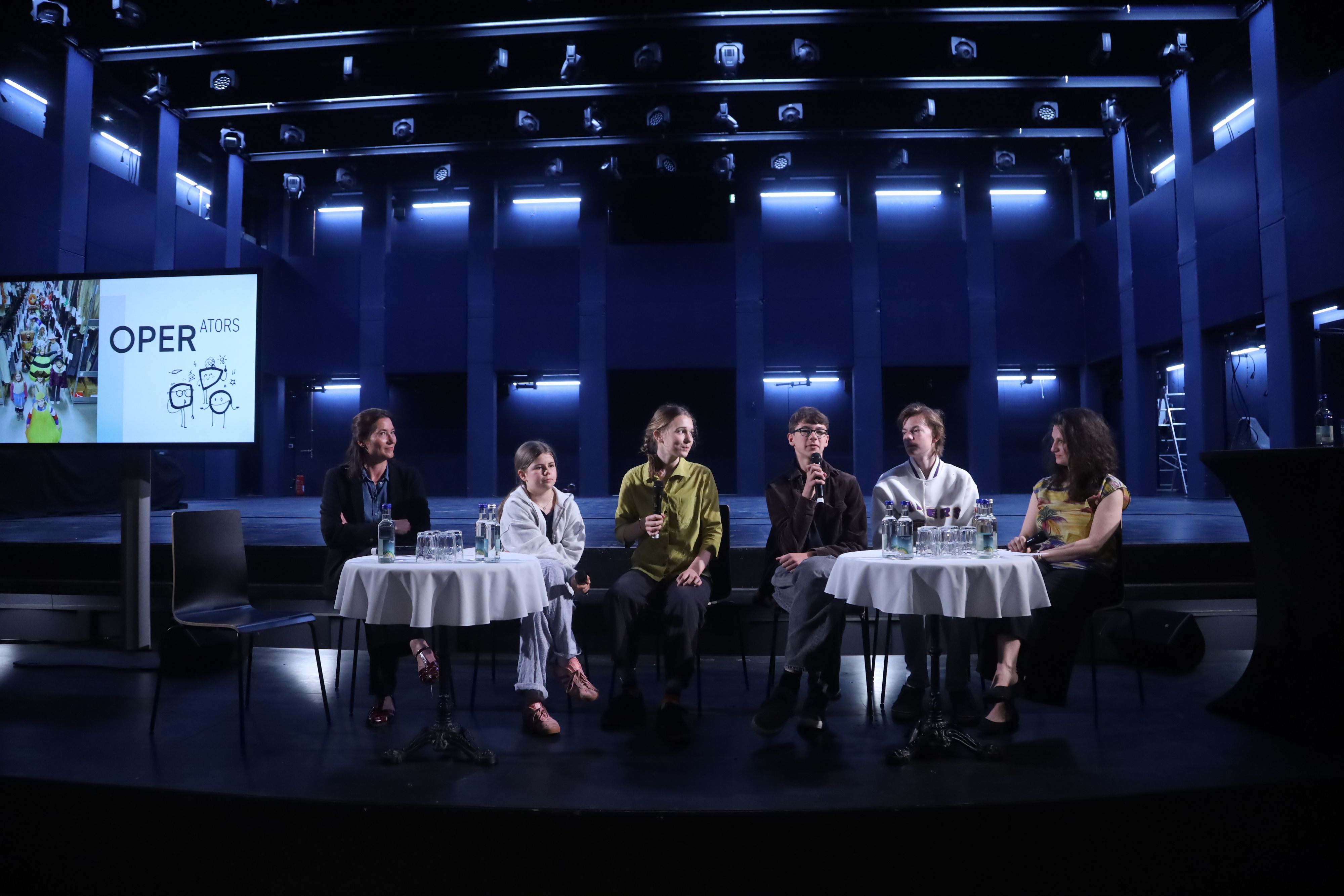 Sechs Menschen sitzen nebeneinander auf einer Bühne und geben eine Pressekonferenz.